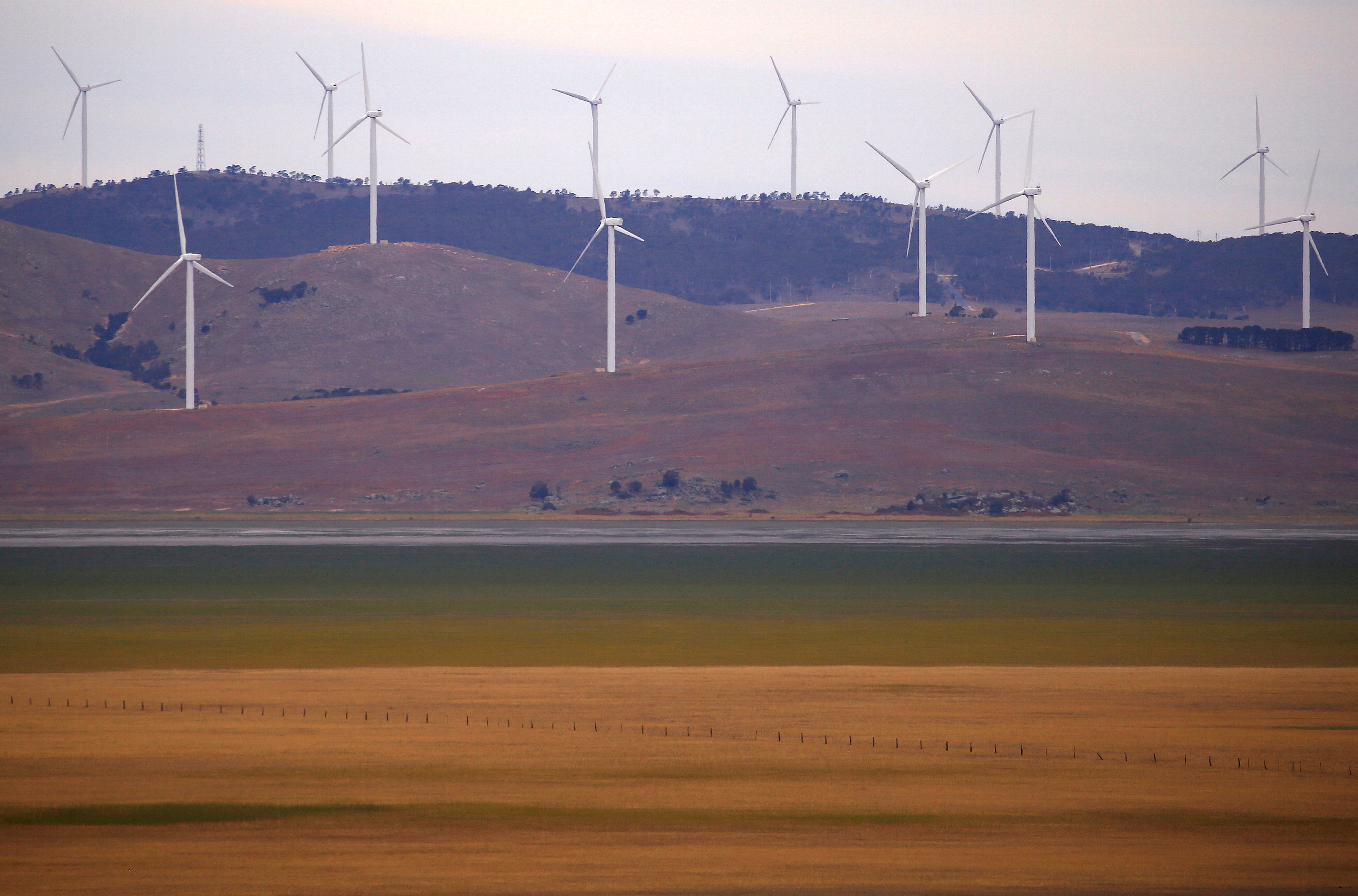 A fence is seen in front of wind turbines that are part of the Infigen Energy Capital Wind Farm located on the hills surrounding Lake George, near the Australian capital city of Canberra