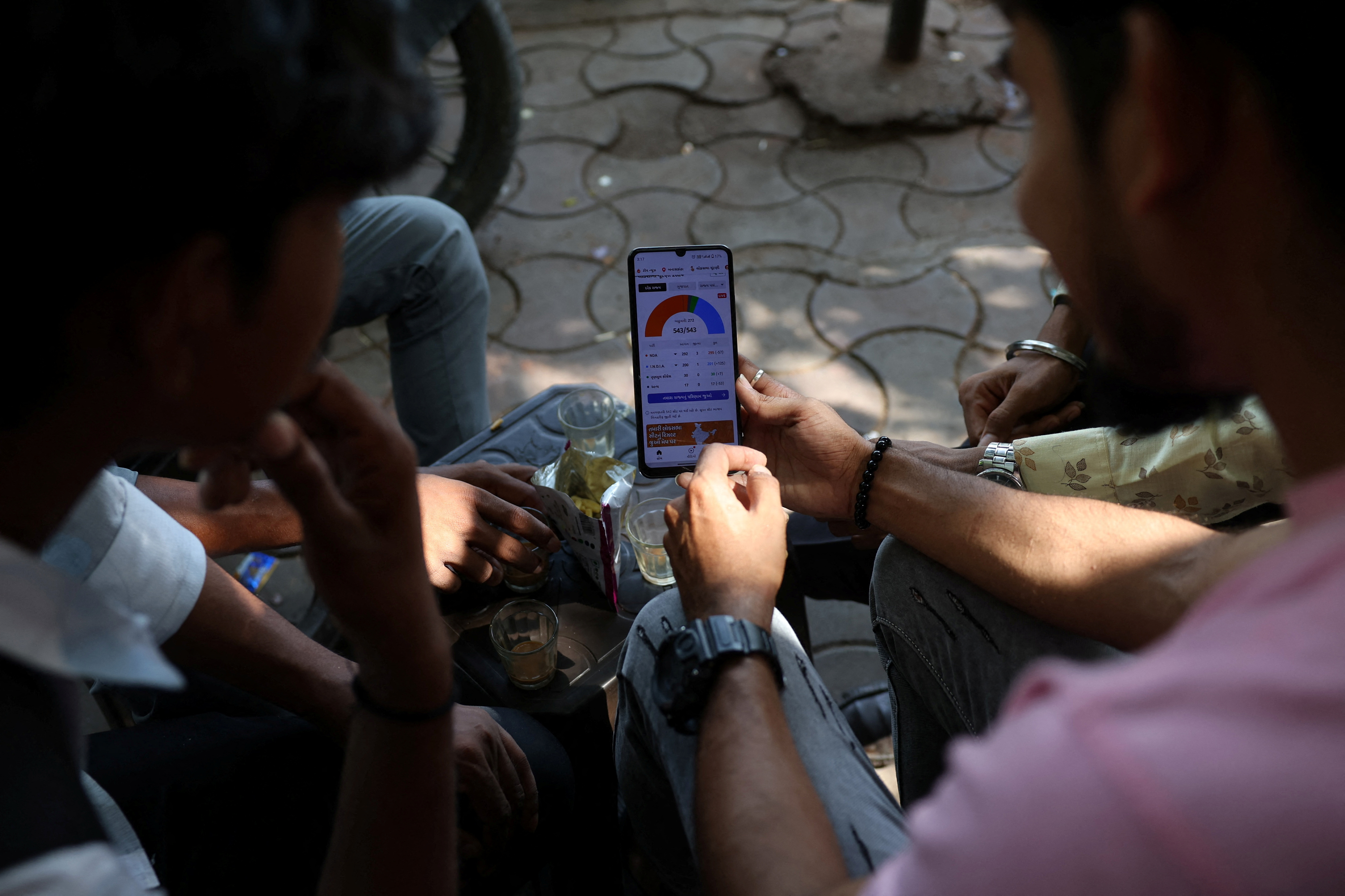 People watch election results on a mobile phone at a roadside tea stall in Ahmedabad