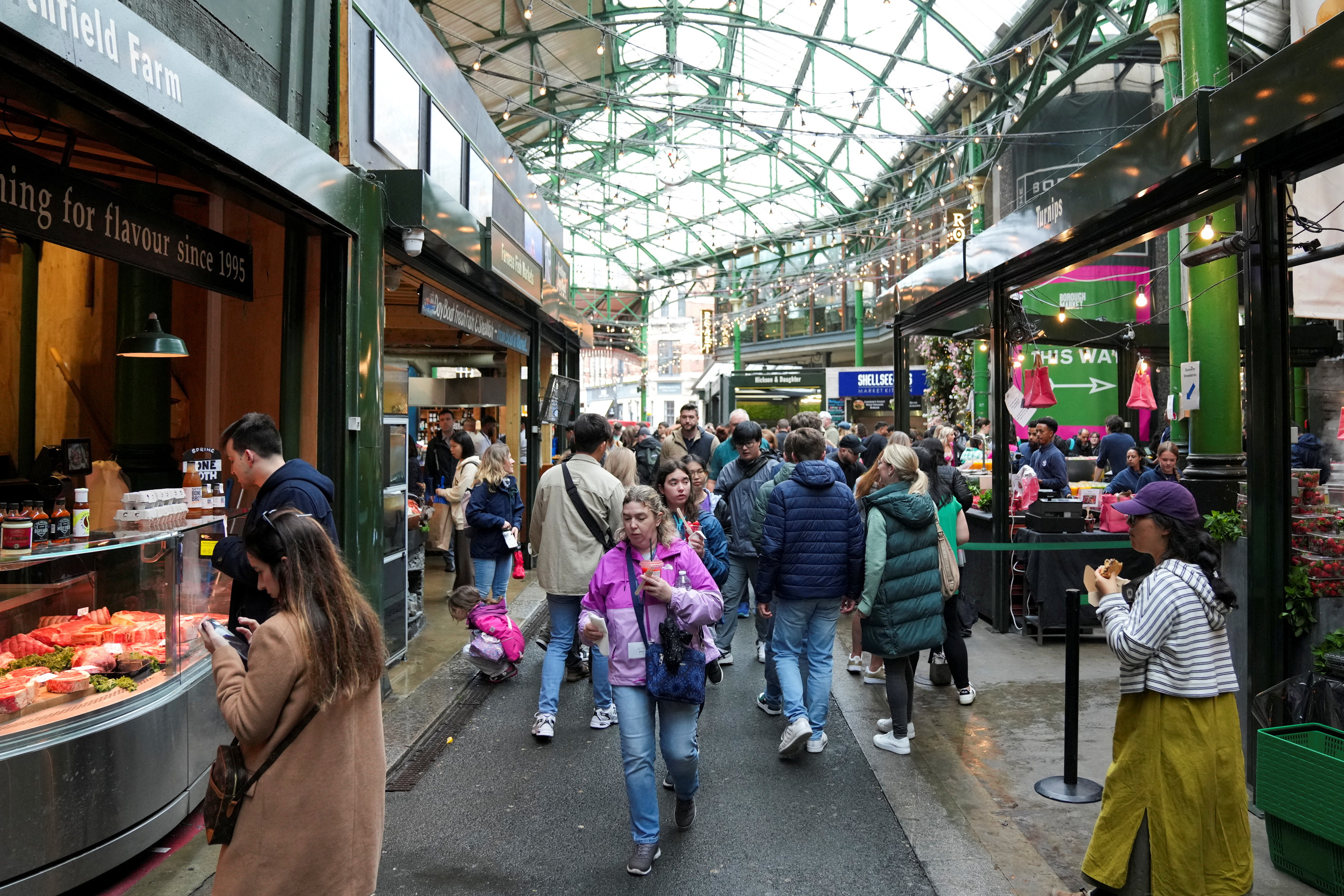 People walk past food stands and market stalls in a Borough Market in London