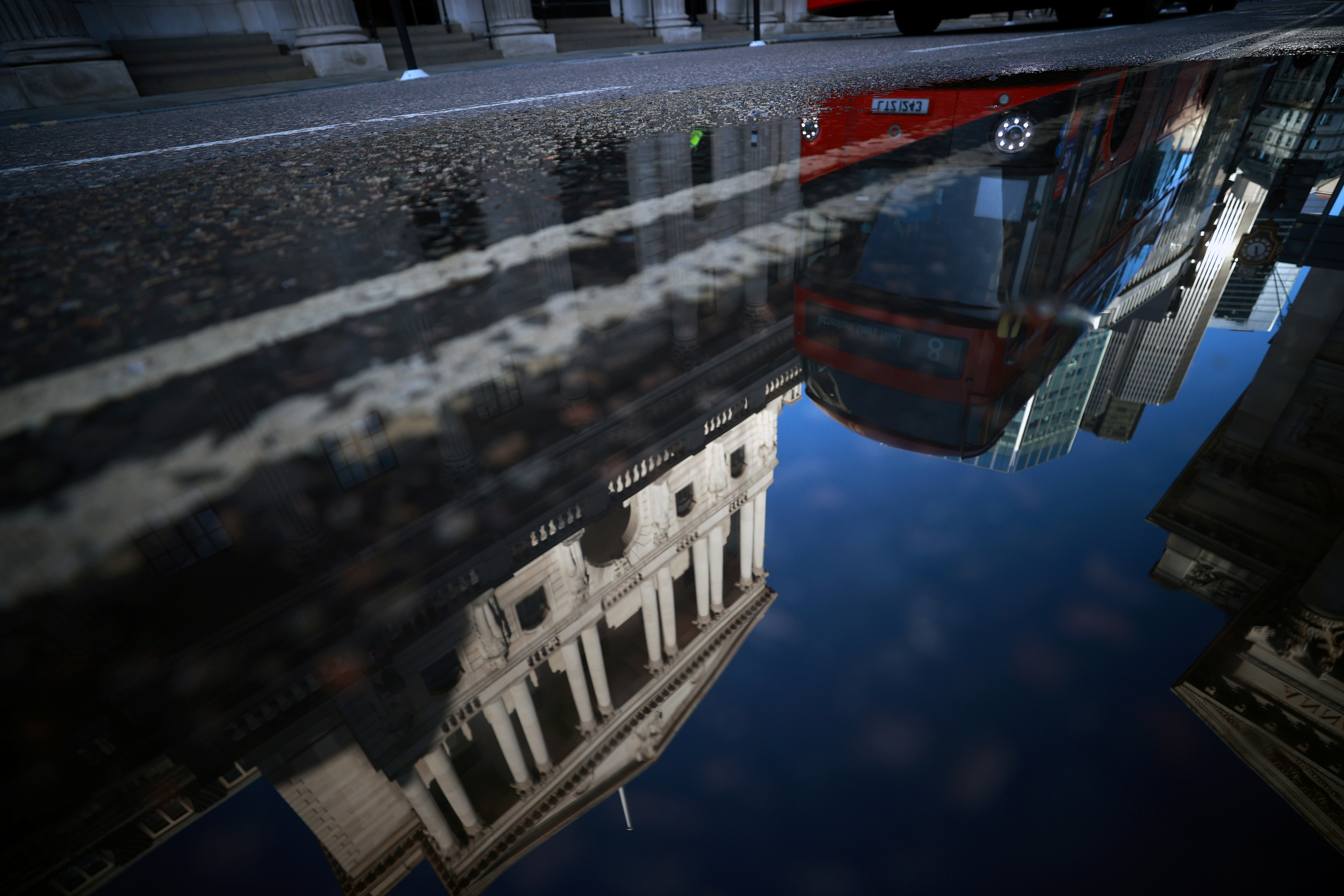 The Bank of England and the City of London financial district are reflected in a puddle, in London