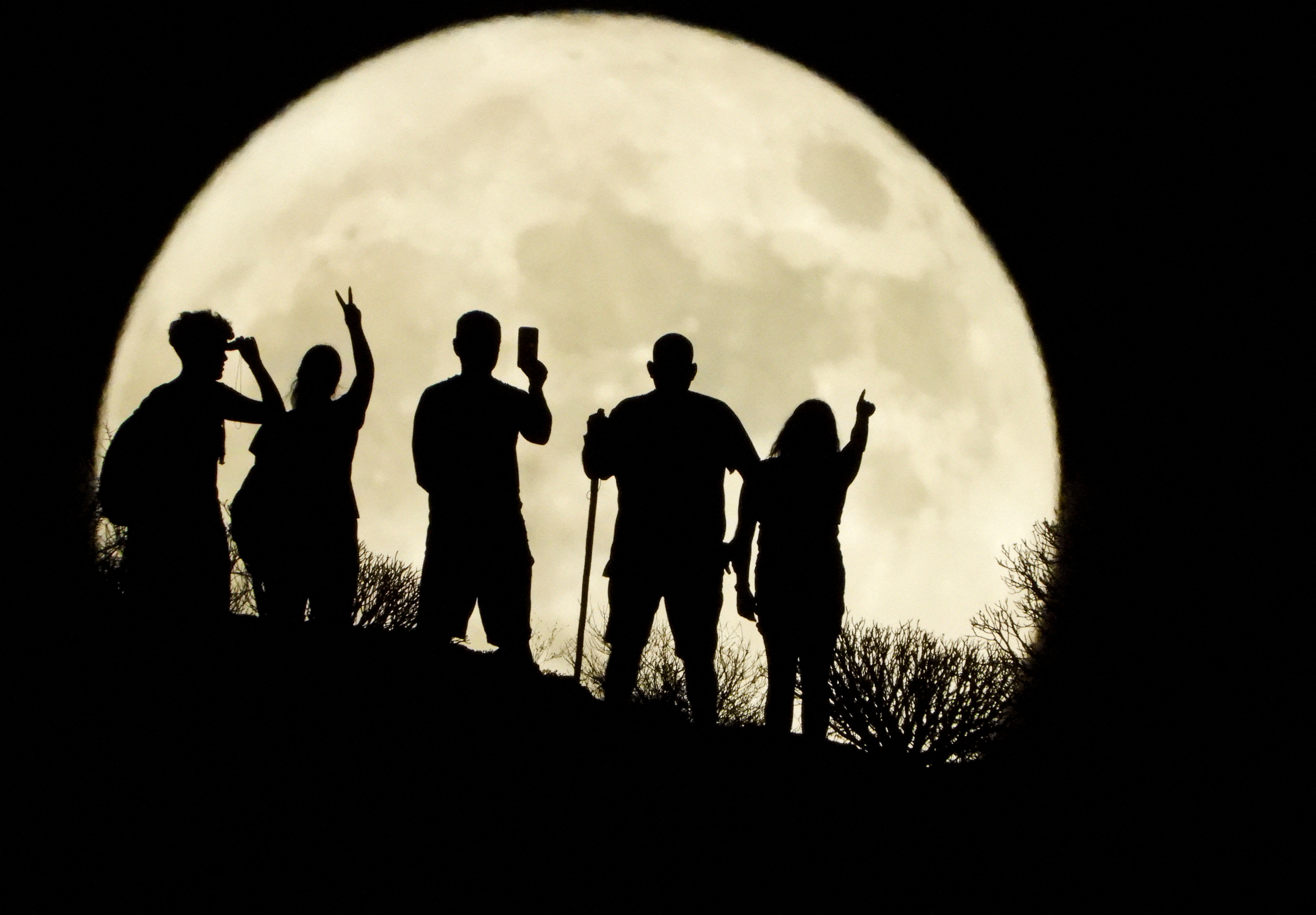 People stand with the full moon known as the 