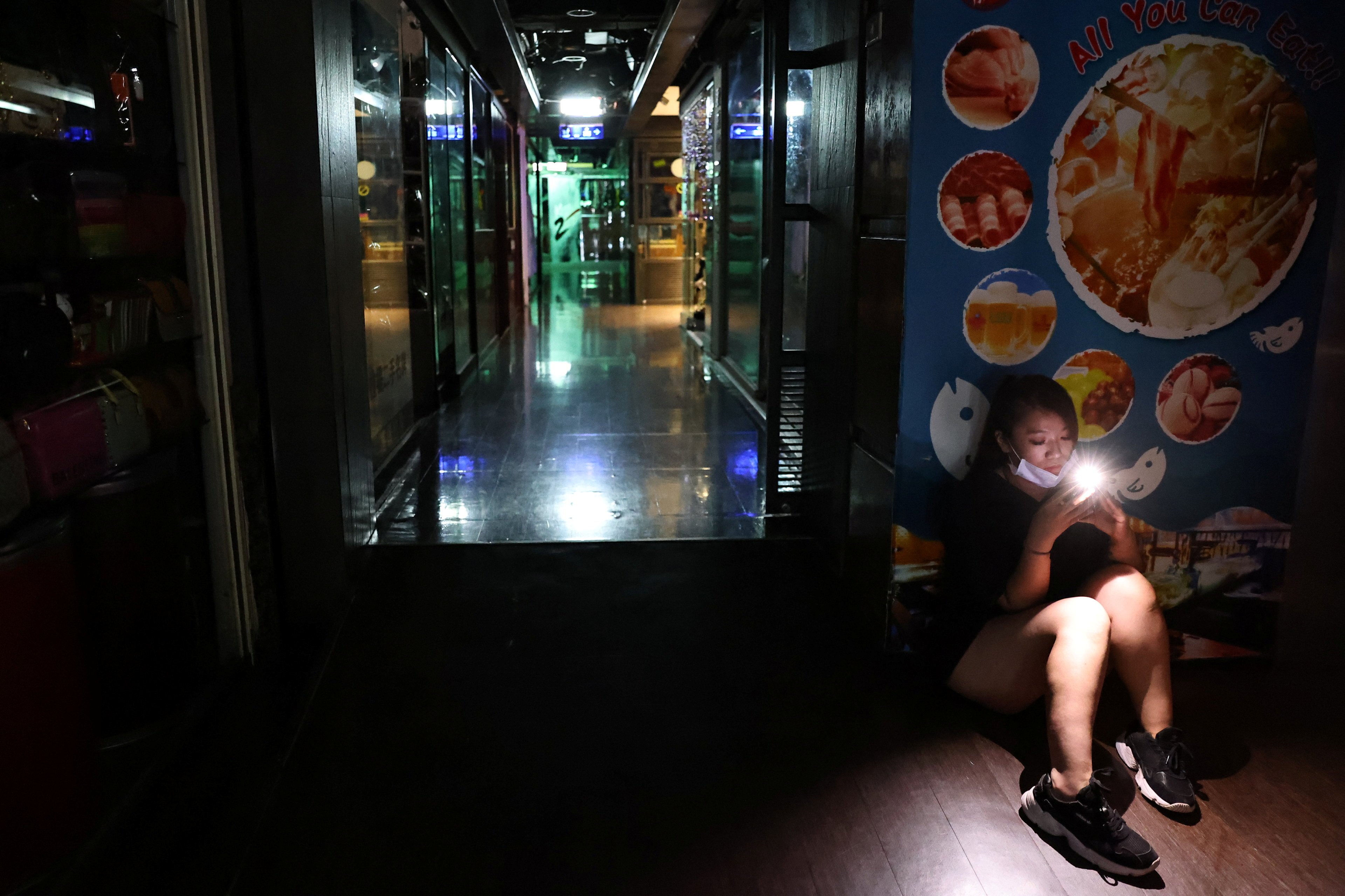 A woman uses her phone while experiencing a blackout due to an outage at a power plant, in Taipei