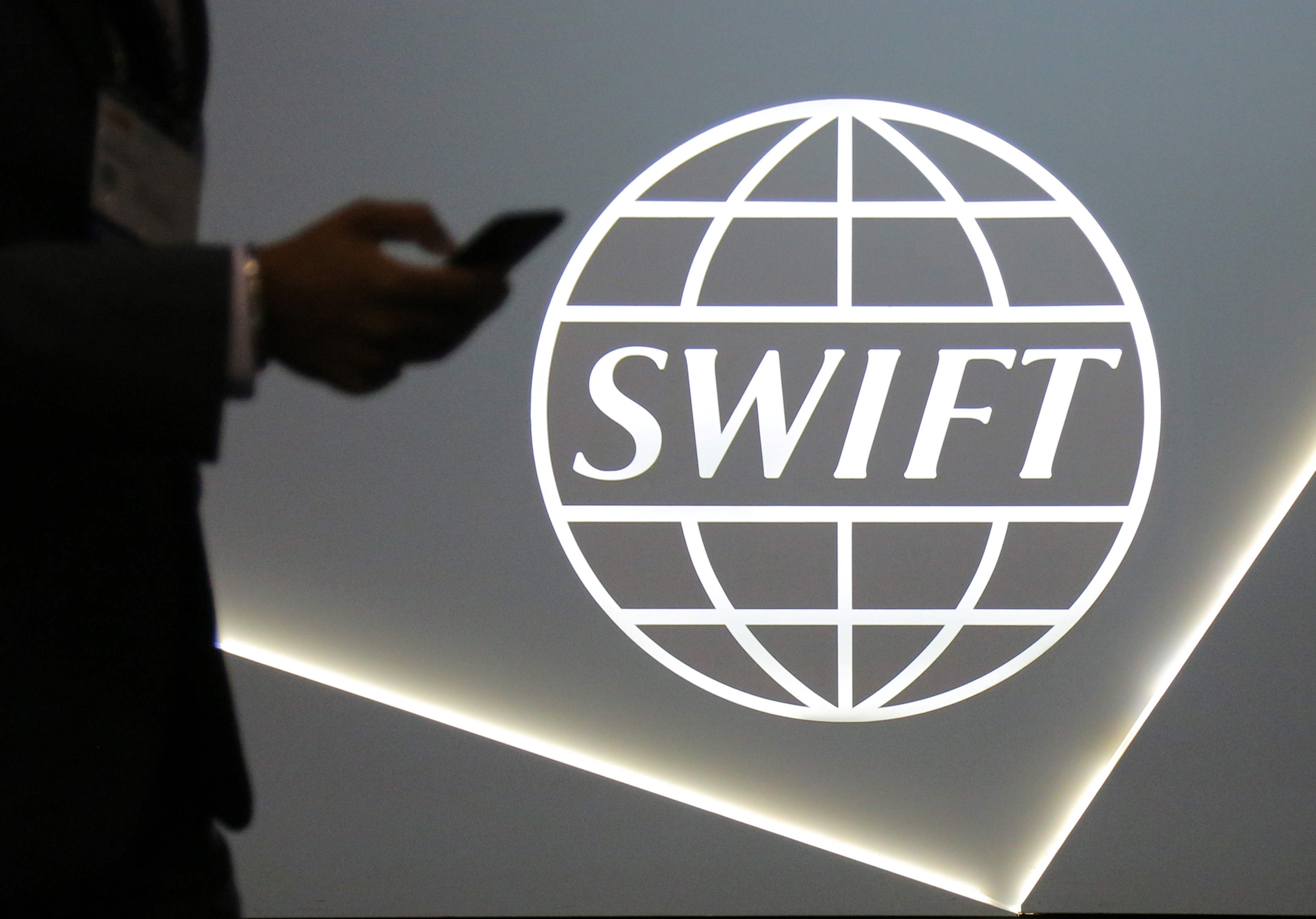 A man using a mobile phone passes the logo of global secure financial messaging services cooperative SWIFT at the SIBOS banking and financial conference in Toronto