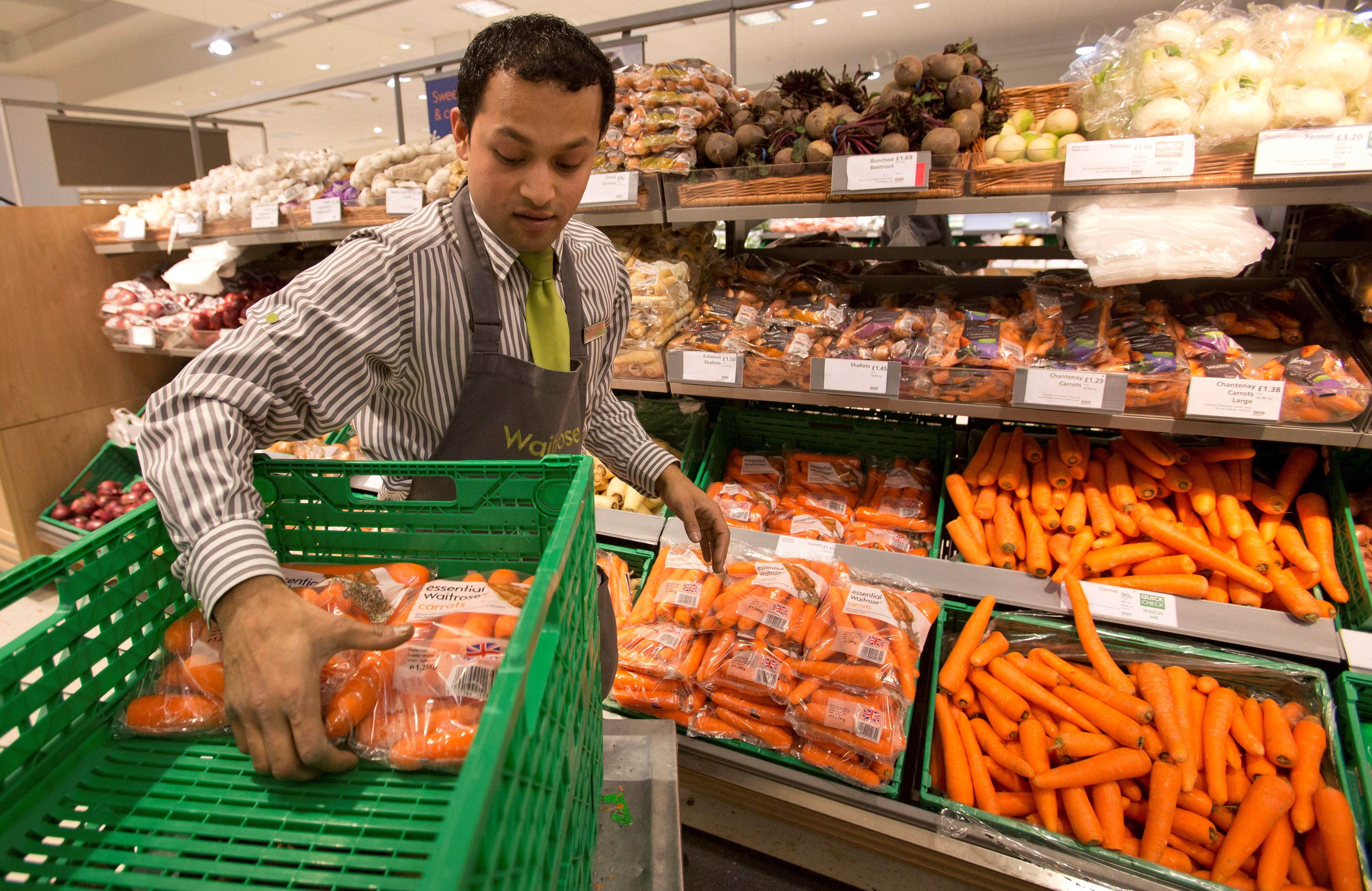 A worker stocks produce shelves in the Canary Wharf store of Waitrose in London