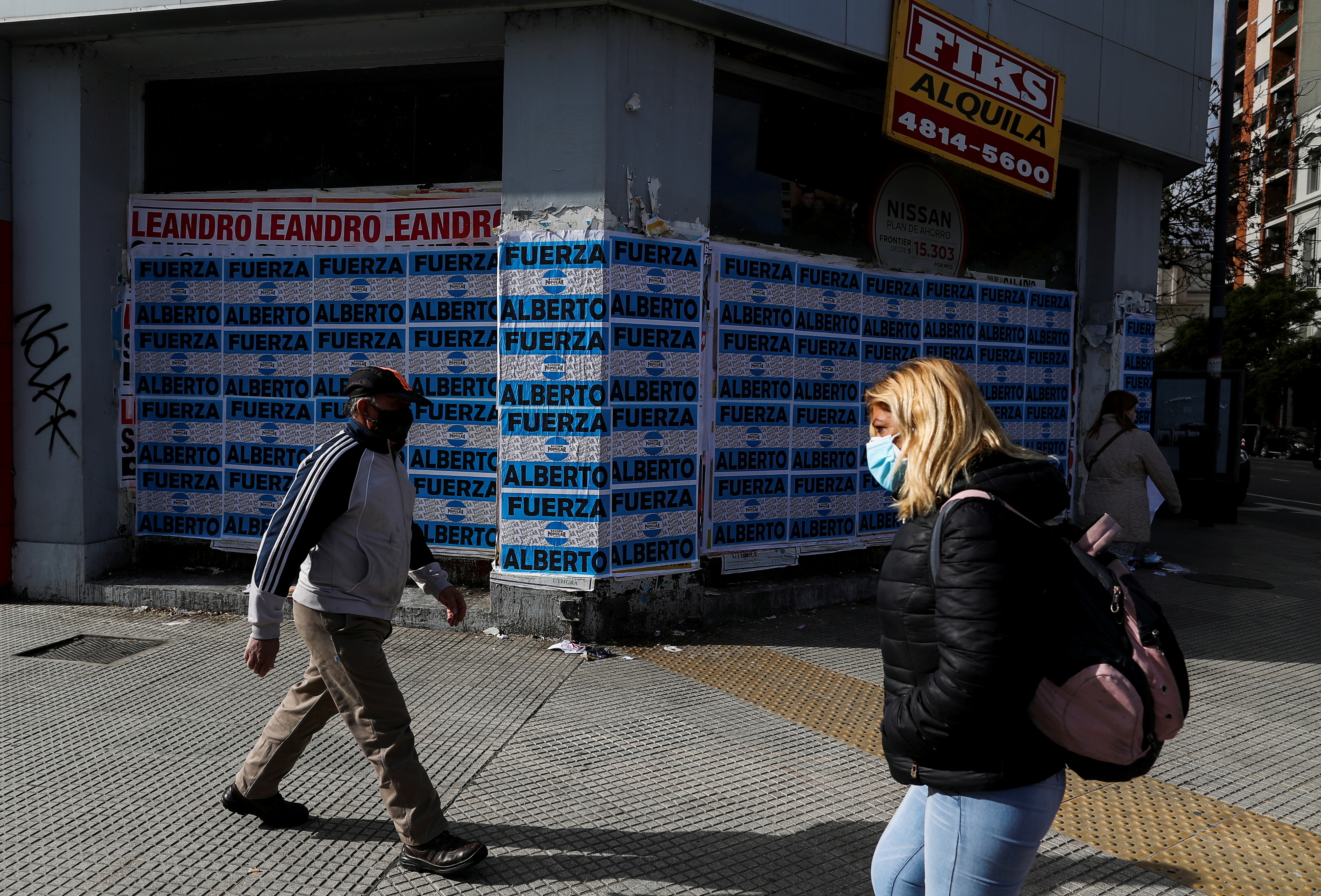 People wearing protective masks walk past an out-of-business store with a sign that reads 