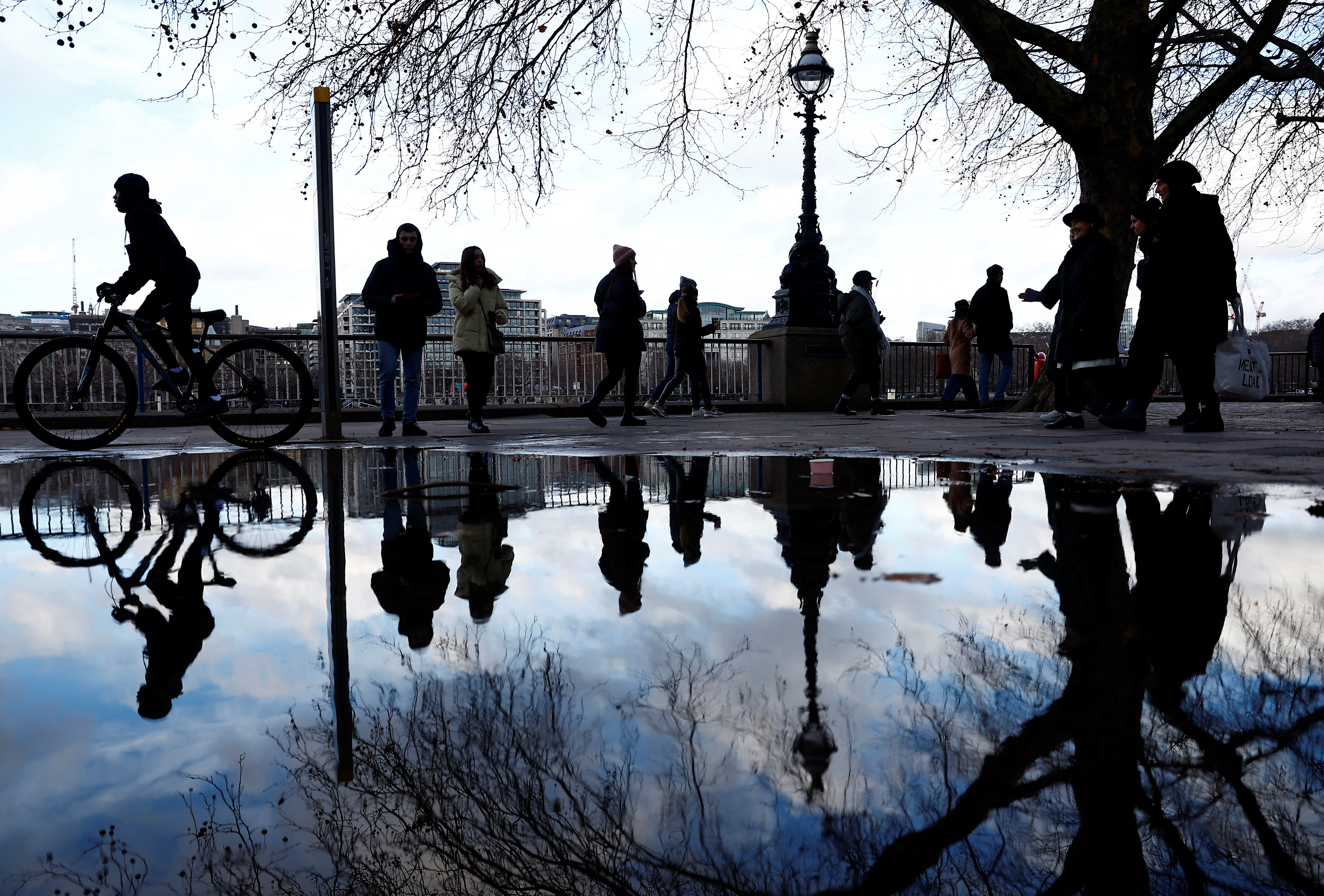 Visitors to the Southbank are seen reflected in rainwater, in London