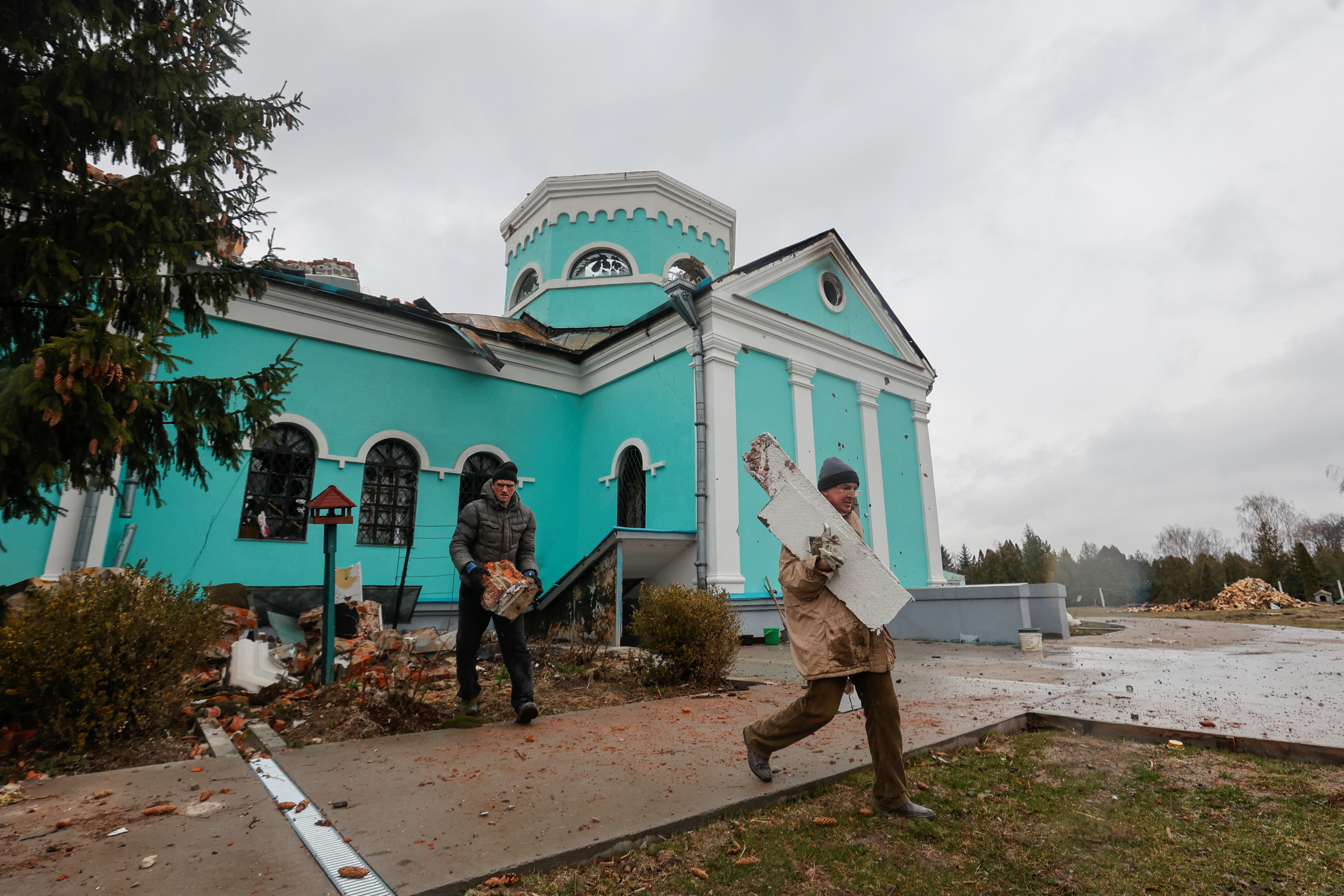 Believers remove debris outside an orthodox church building damaged by heavy shelling in Chernihiv