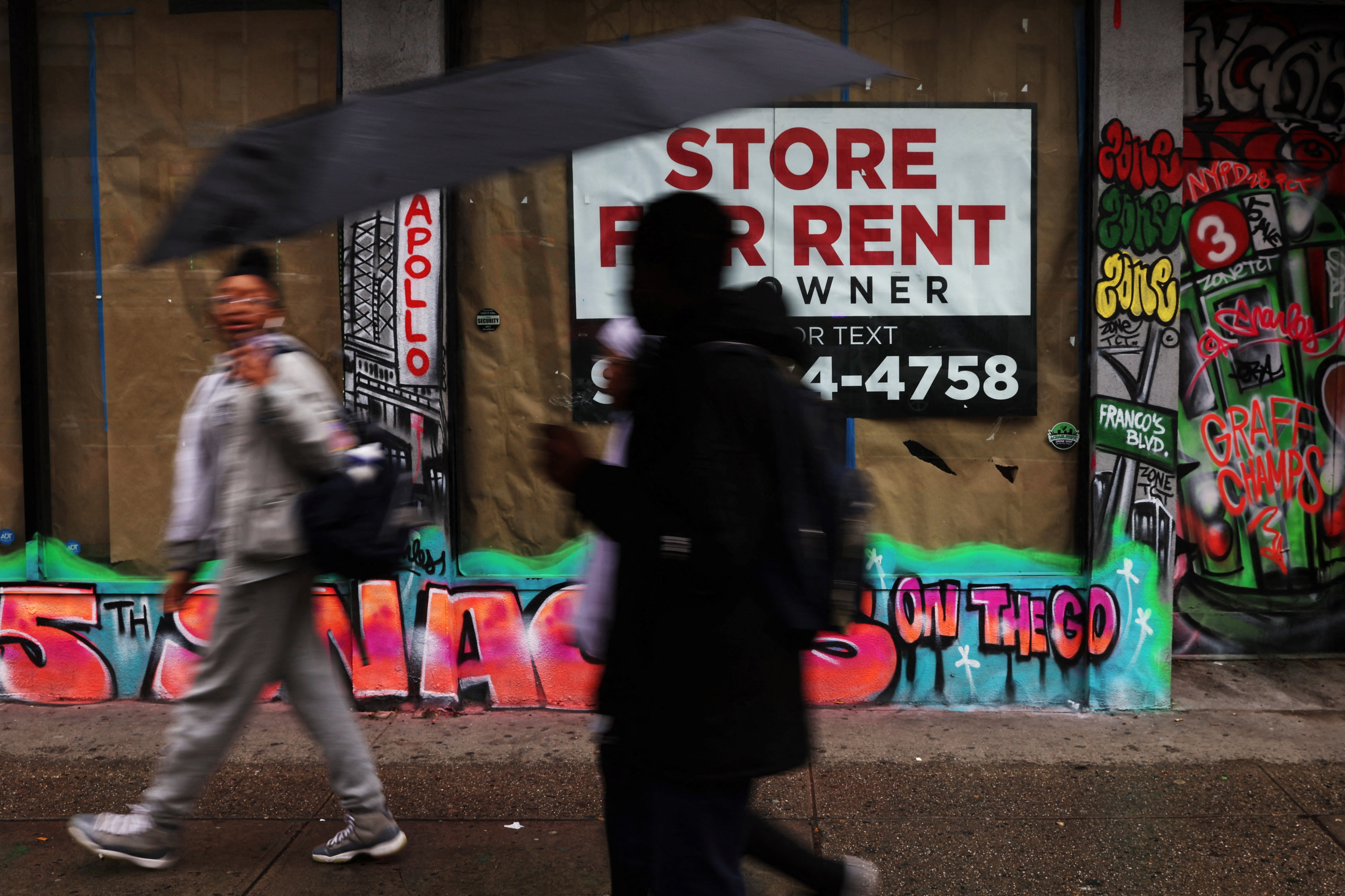 People walk in the rain by commercial real estate for rent along 125th street in the Harlem area of New York City