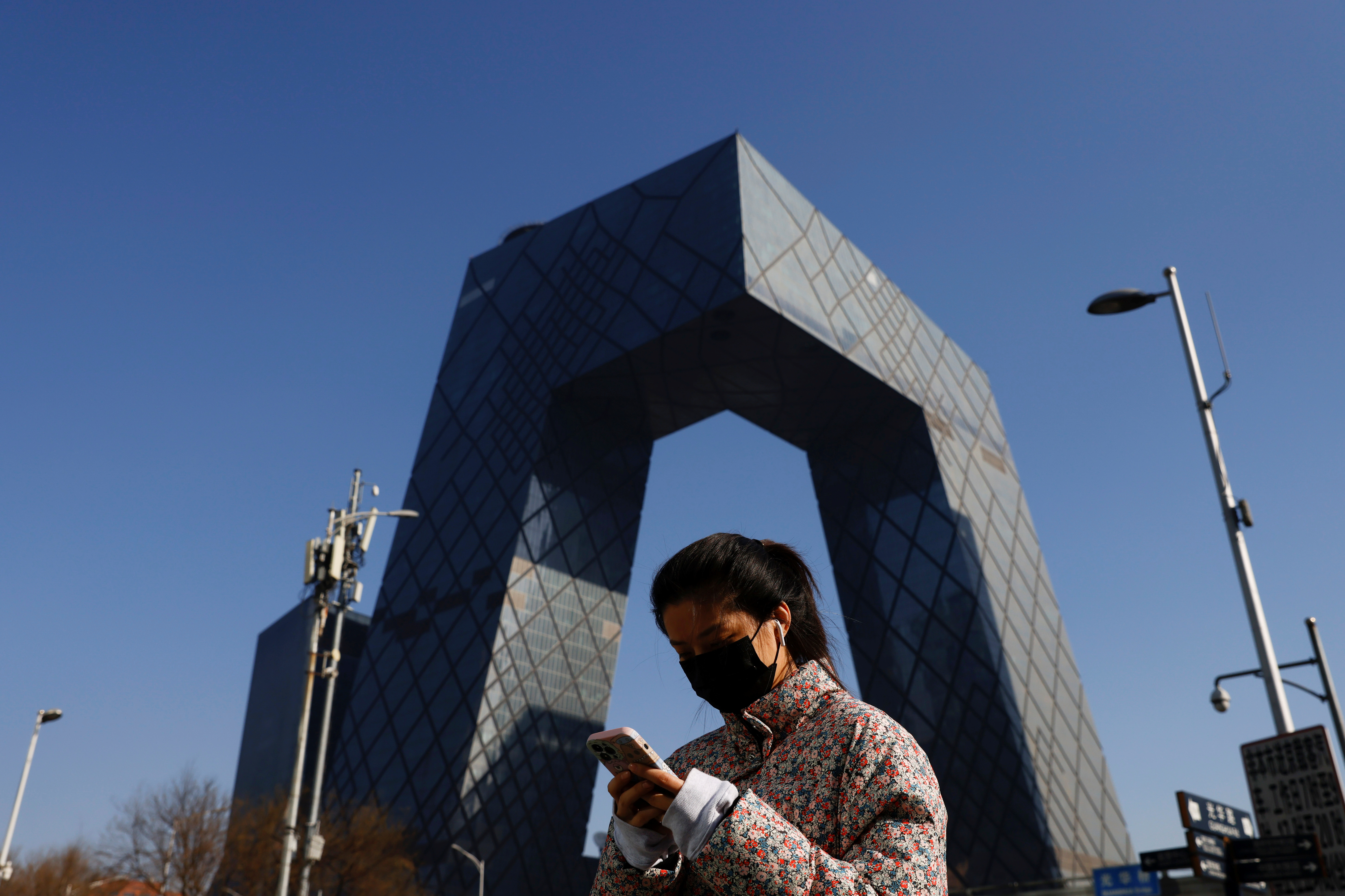 A woman holding a mobile phone walks past the CCTV headquarters, the home of Chinese state media outlet CCTV and its English-language sister channel CGTN, in Beijing, China February 5, 2021. REUTERS/Carlos Garcia Rawlins