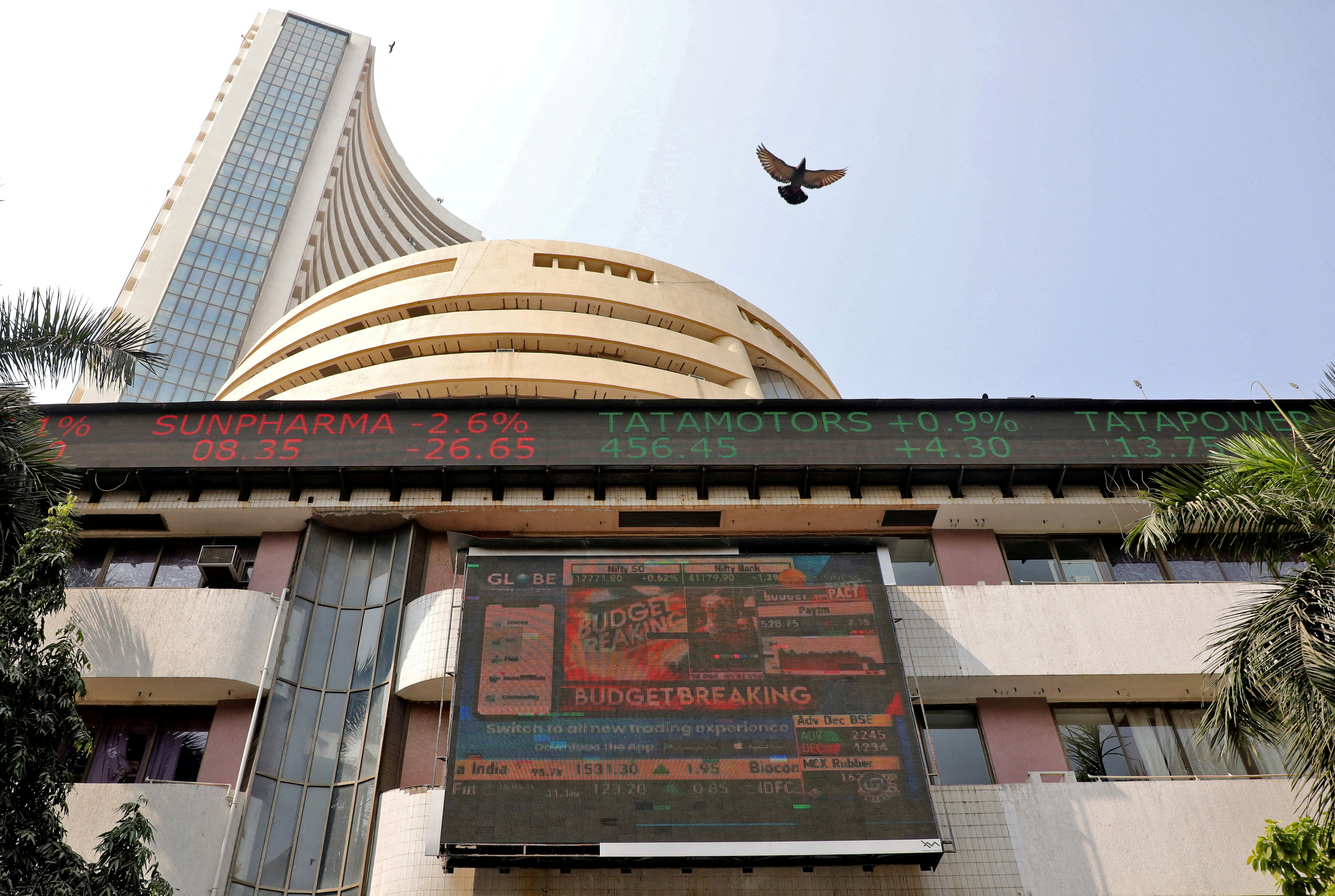 A bird flies past a screen displaying the Sensex results on the facade of BSE building in Mumbai