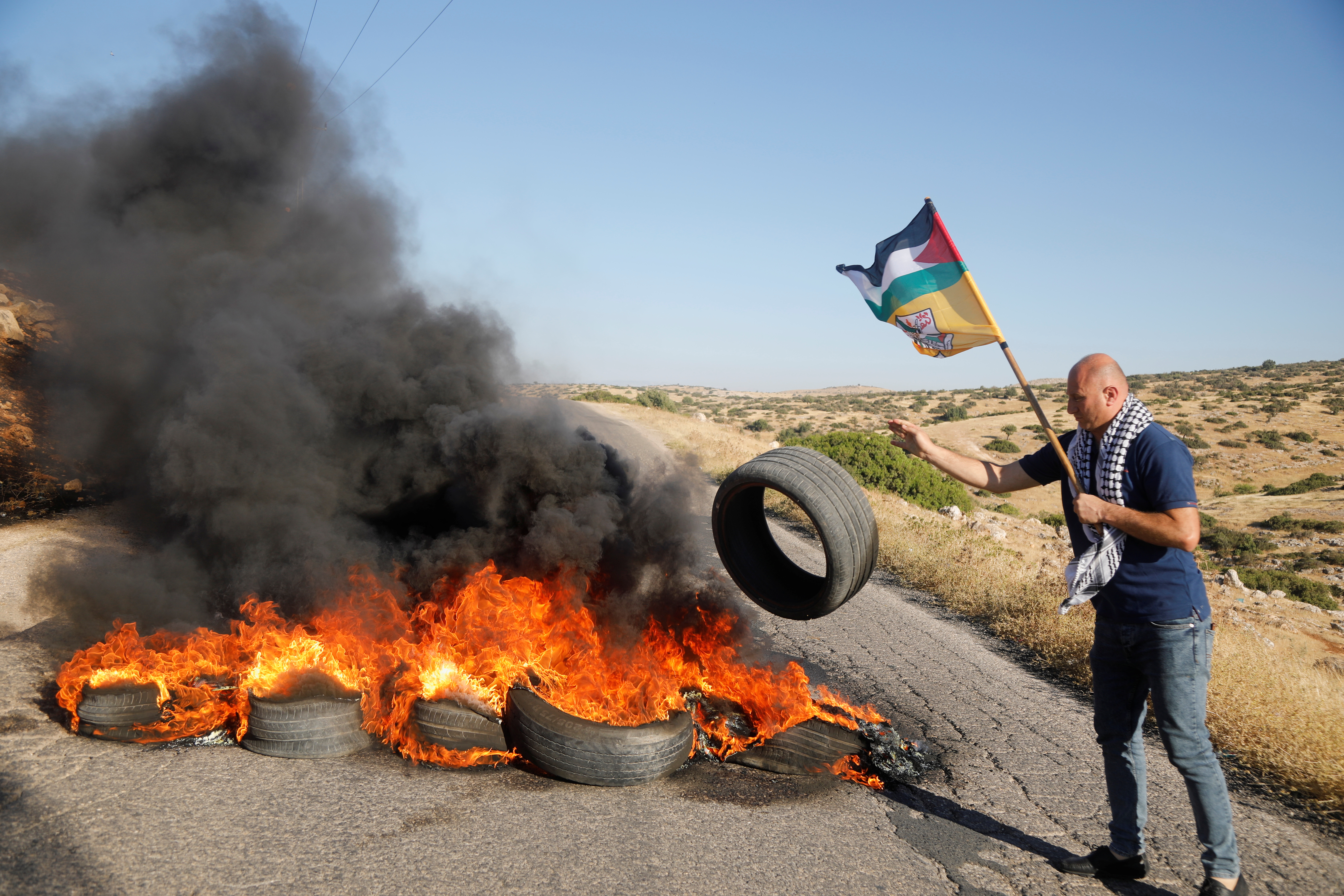 A Palestinian demonstrator throws a tire to a burning barricade, following a flare-up of Israeli-Palestinian violence, on a road near Tubas in the Israeli-occupied West Bank, May 15, 2021. REUTERS/Raneen Sawafta