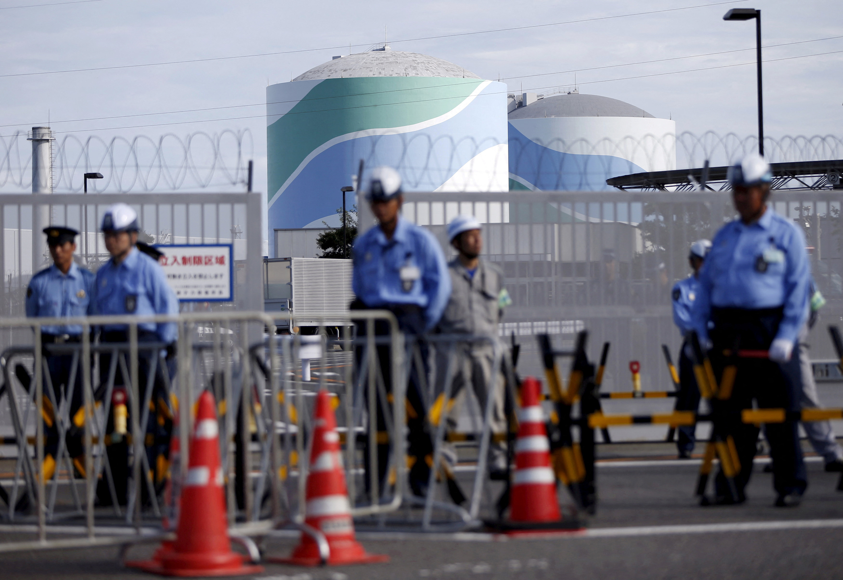 Security personnel stand guard in front of an entrance gate of Kyushu Electric Power's Sendai nuclear power station in Satsumasendai, Japan
