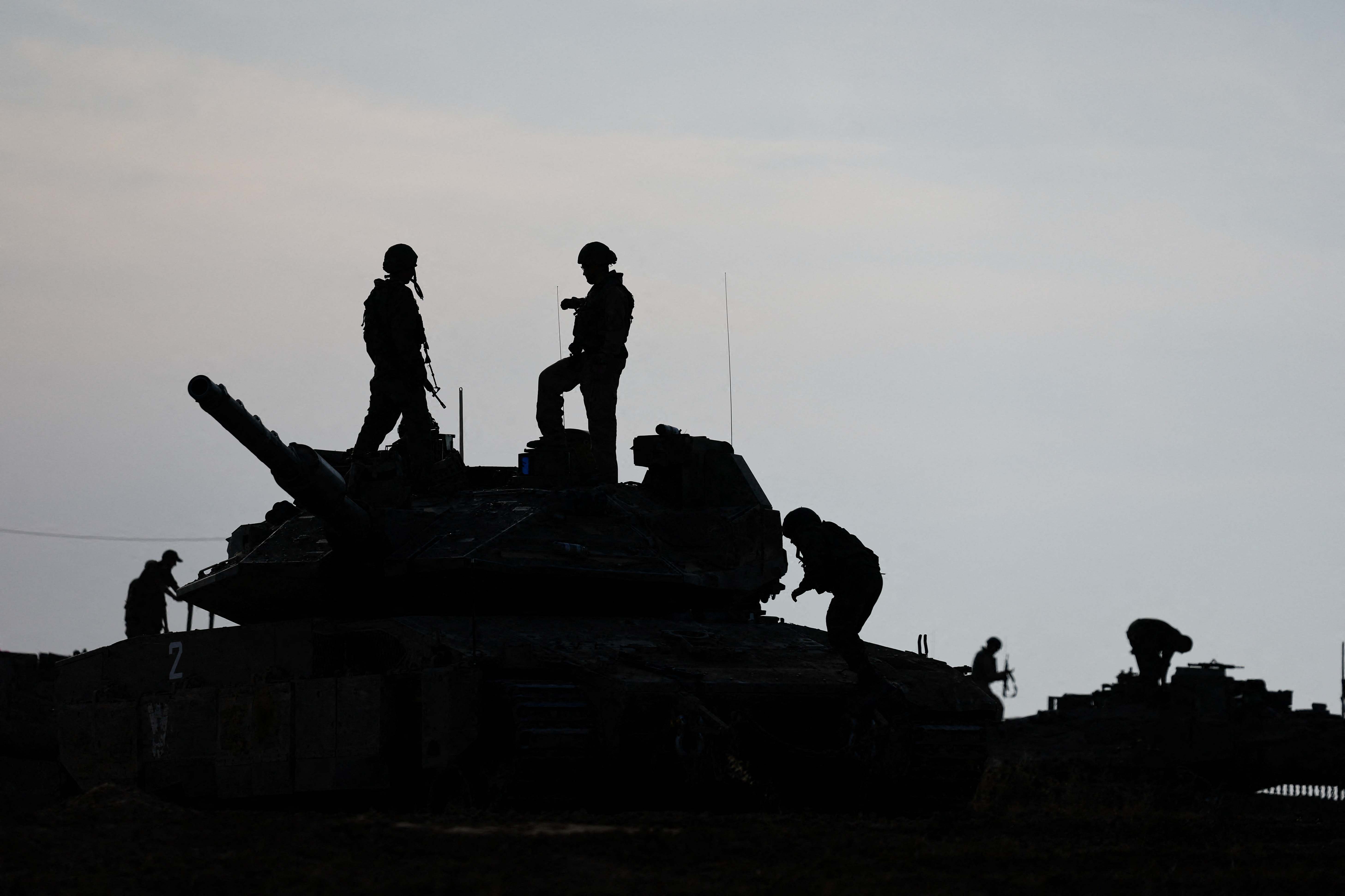 Israeli soldiers are silhouetted as they stand on a tank, near the Israel-Gaza border