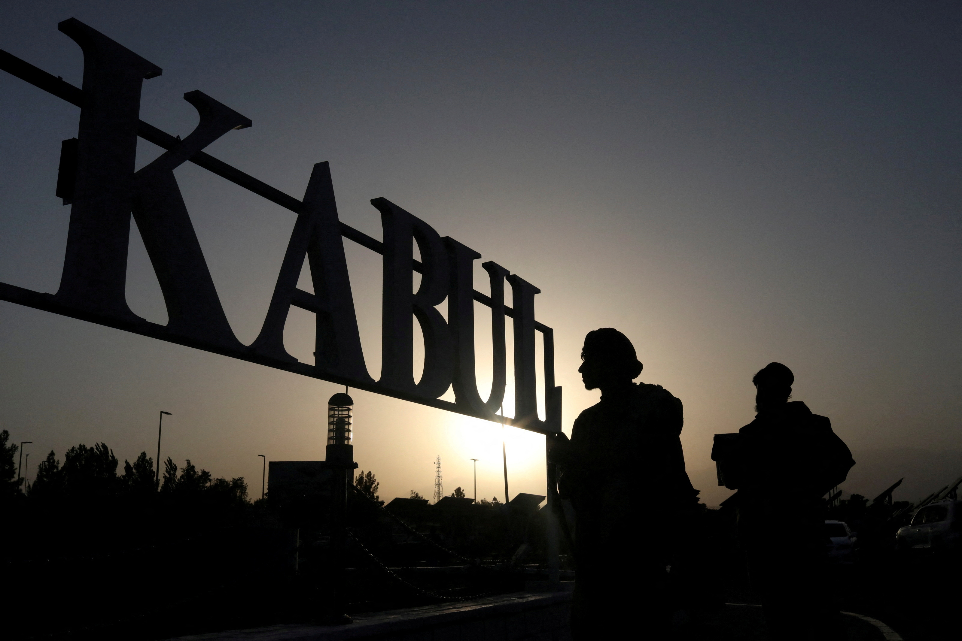 Taliban soldiers stand in front of a sign at the international airport in Kabul