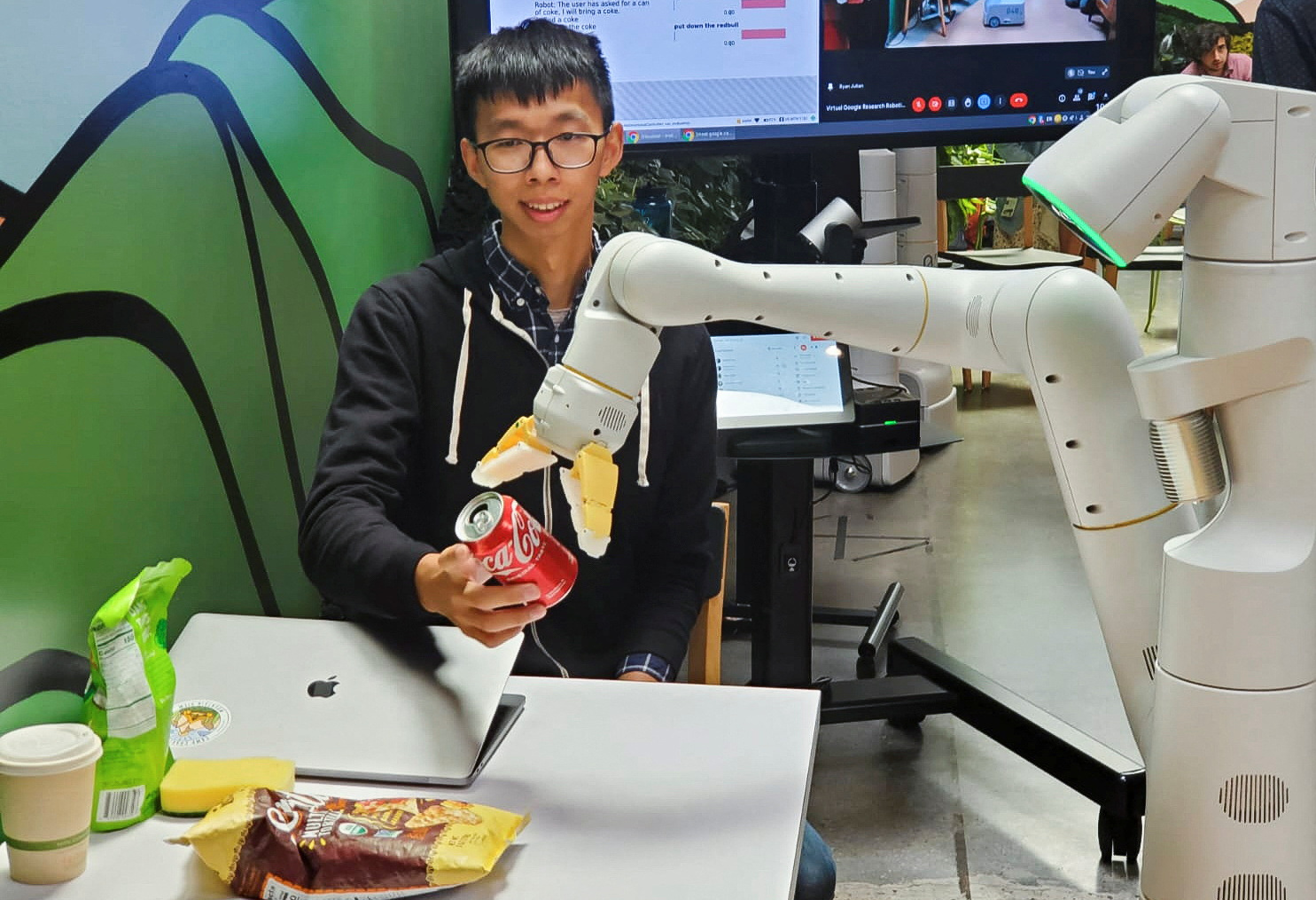Google research scientist Fei Xia accepts a Coca-Cola can from a robot during a demonstration of AI technology at a company micro-kitchen in Mountain View