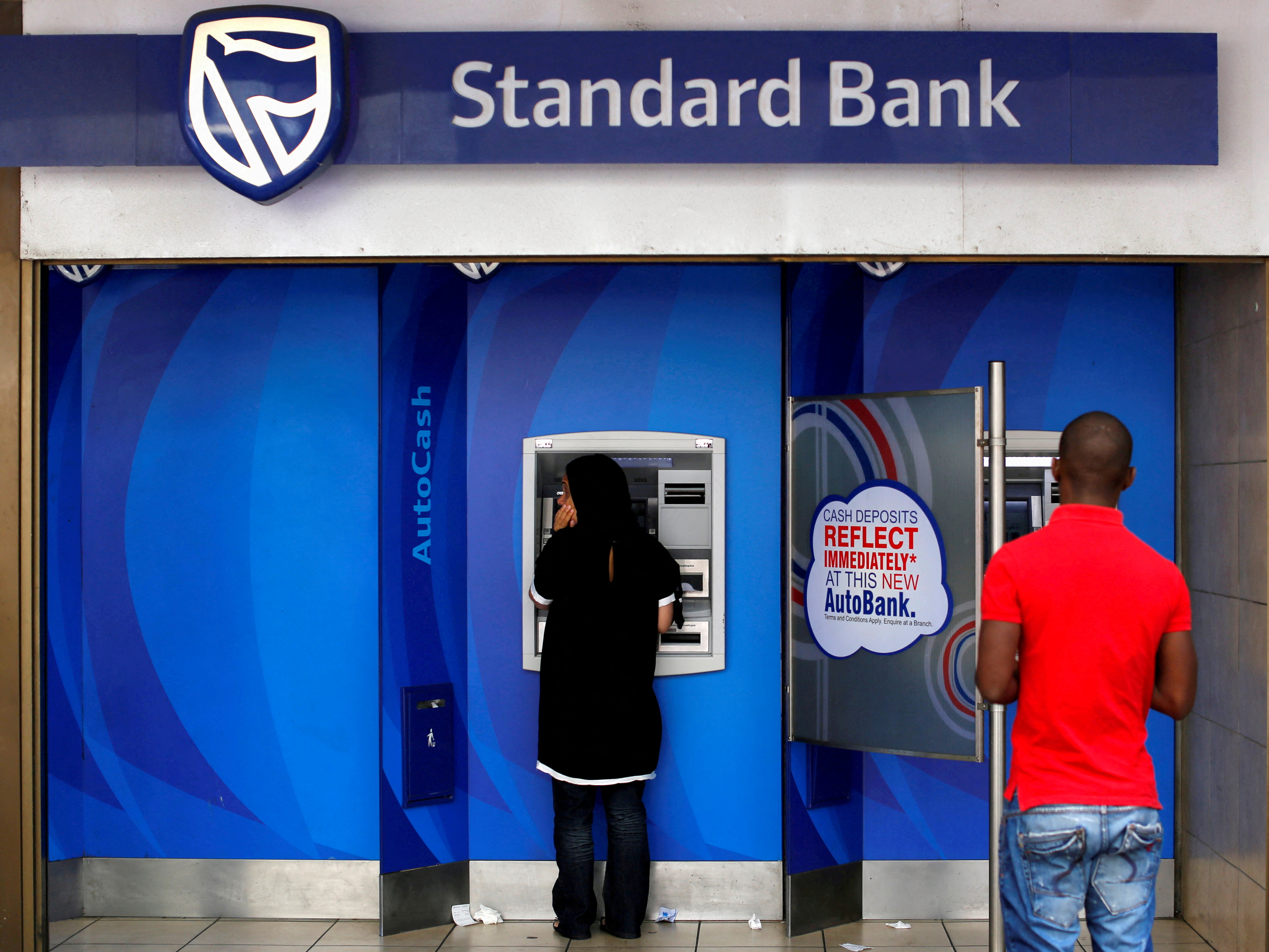 Customers queue to draw money from an ATM outside a branch of South Africa's Standard Bank in Cape Town