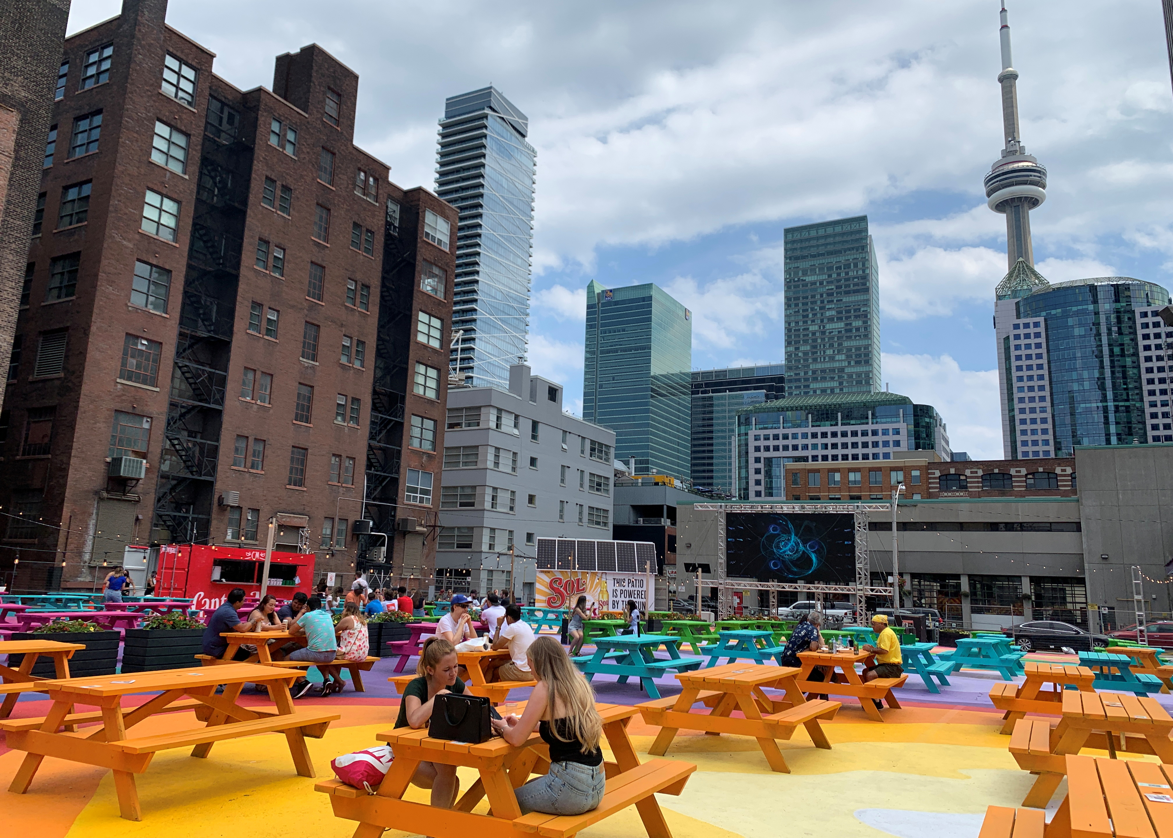People sit at multi-coloured picnic tables in the RendezViews outdoor patio project in Toronto