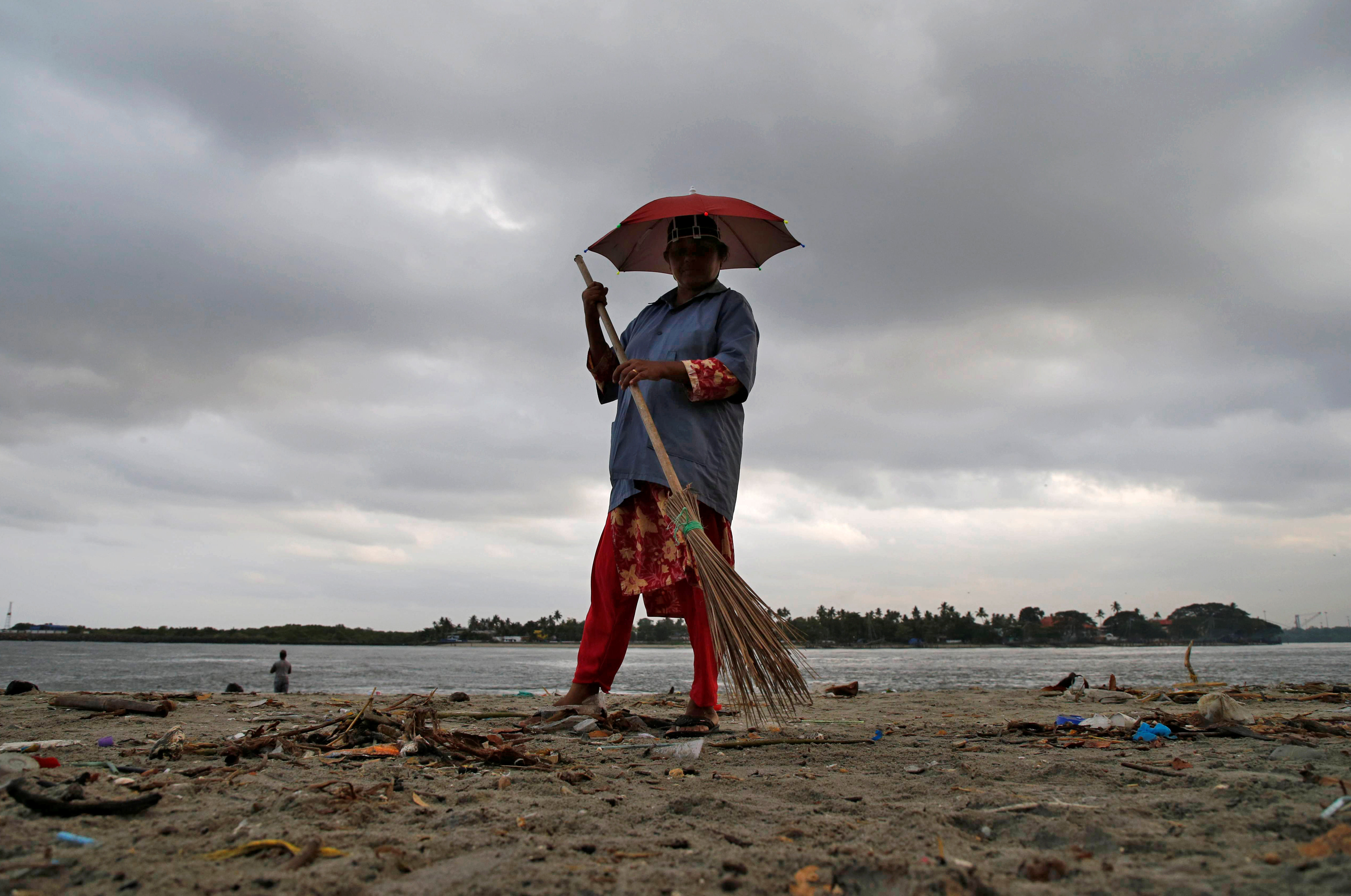 A worker cleans a beach in the backdrop of pre-monsoon clouds at Fort Kochi beach in Kochi