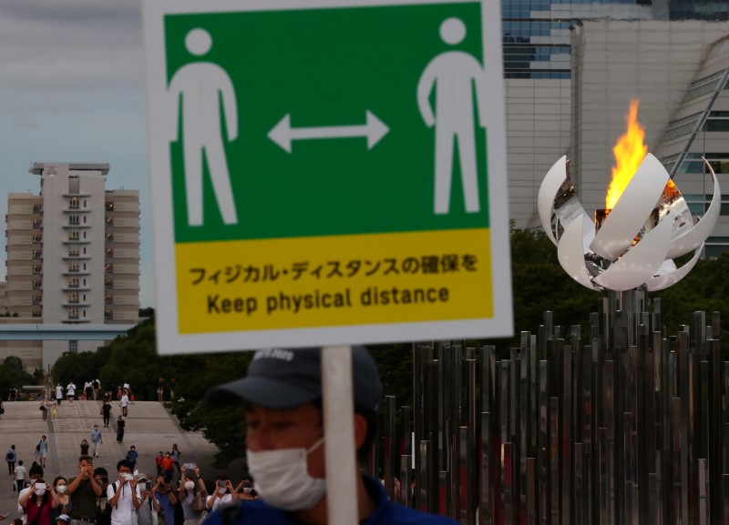 A staff wearing a protective mask, amid the coronavirus disease (COVID-19) outbreak, holds a social distance sign in front of the second Olympic flame cauldron of Tokyo 2020 Olympic Games in Tokyo, Japan, August 7, 2021.  REUTERS/Kim Kyung-Hoon