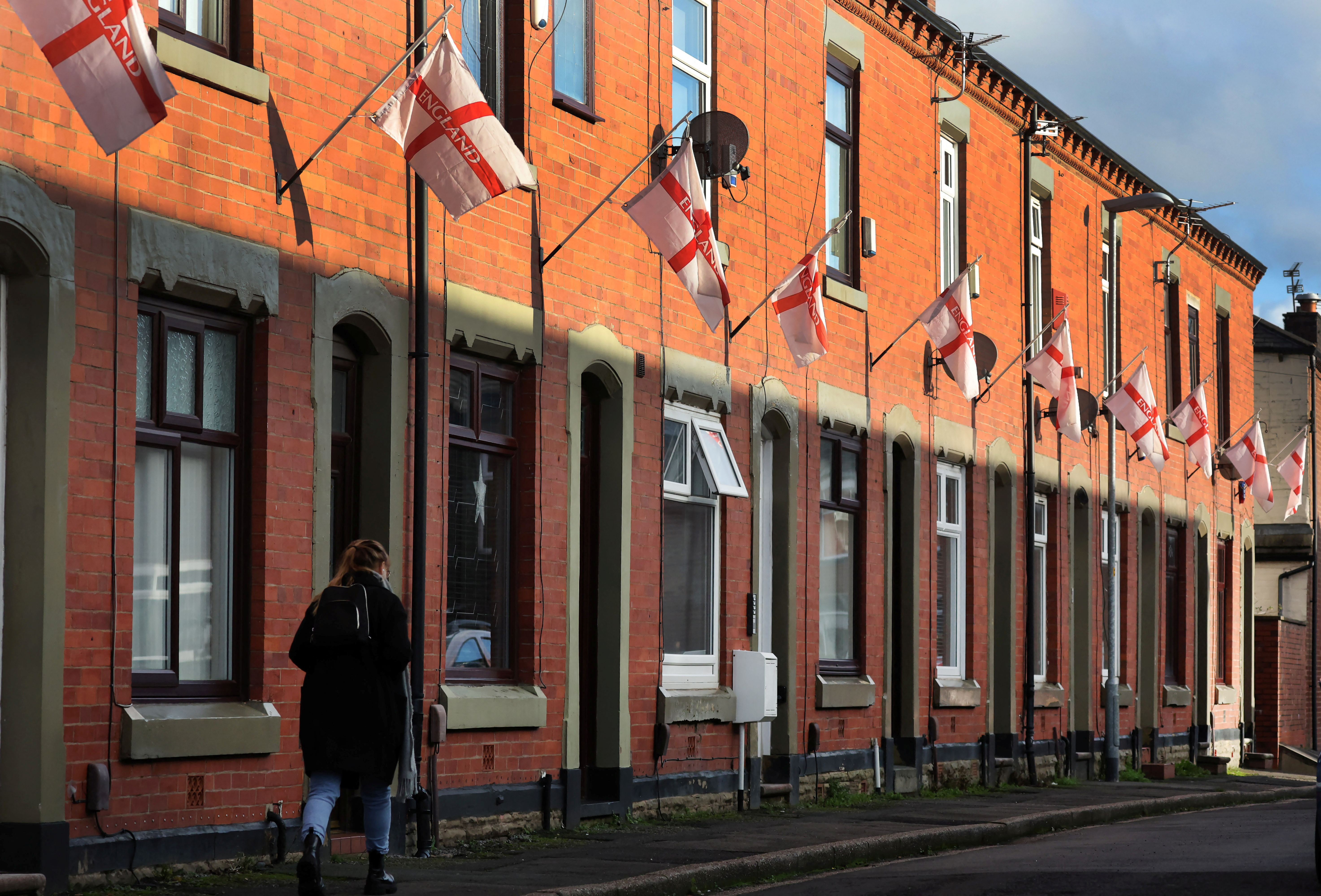 A woman walks past English flags as they hang outside houses on Wales Street in Oldham