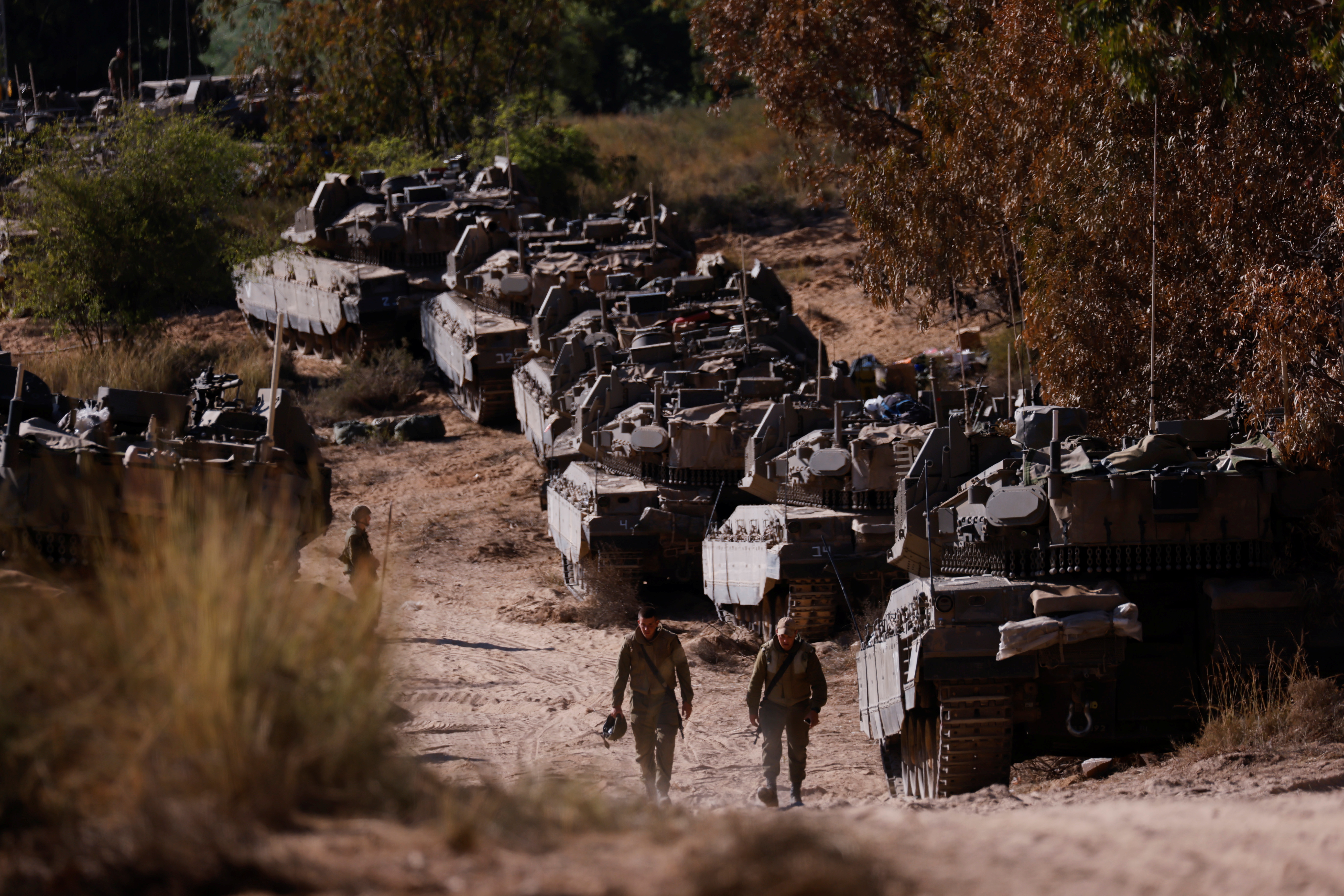Israeli soldiers walk next to tanks near the border between Israel and the Gaza Strip, on its Israeli side