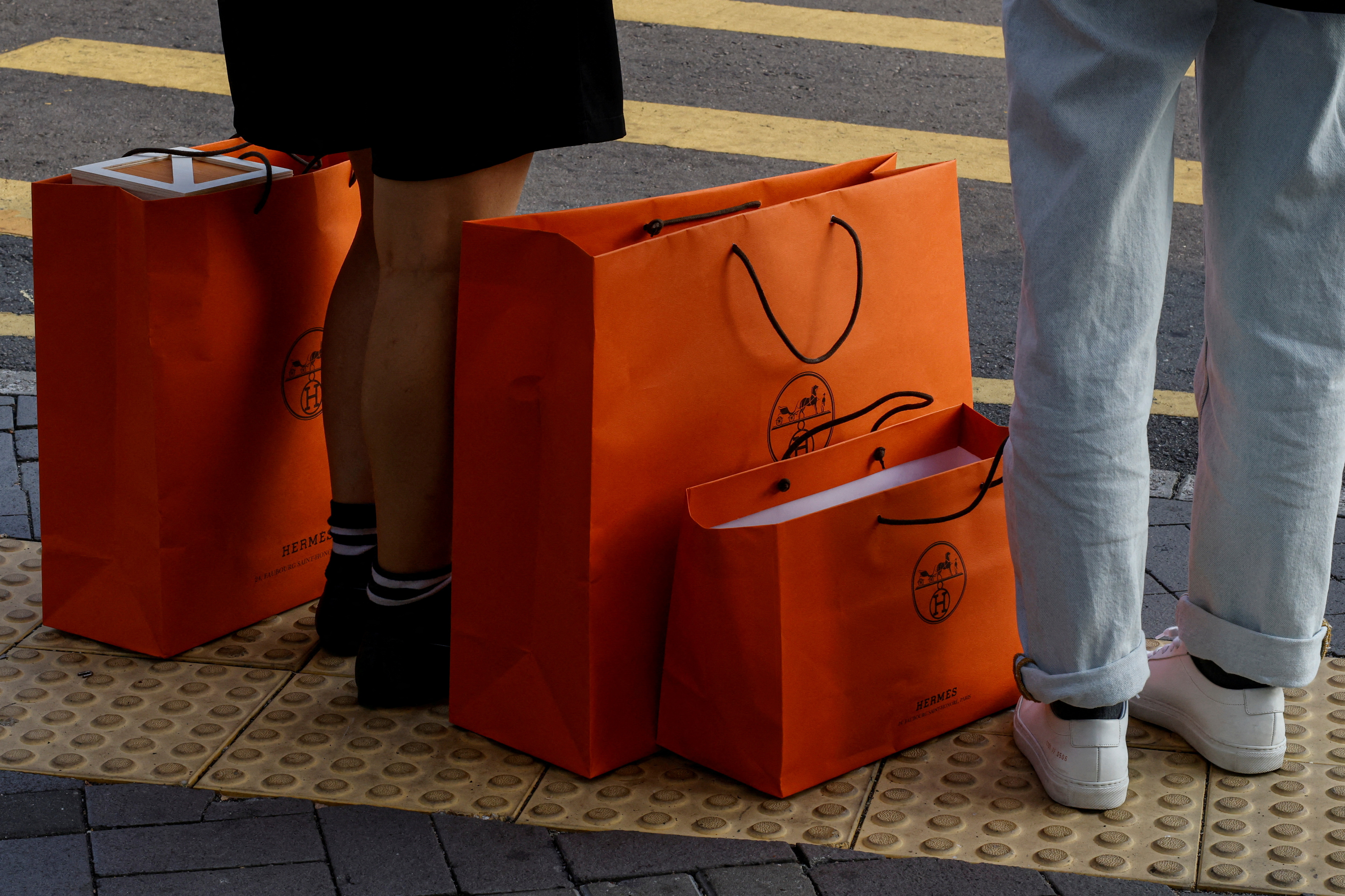 People stand with Hermes shopping bags as they wait at a traffic light in Tsim Sha Tsui, a bustling shopping hotspot, in Hong Kong