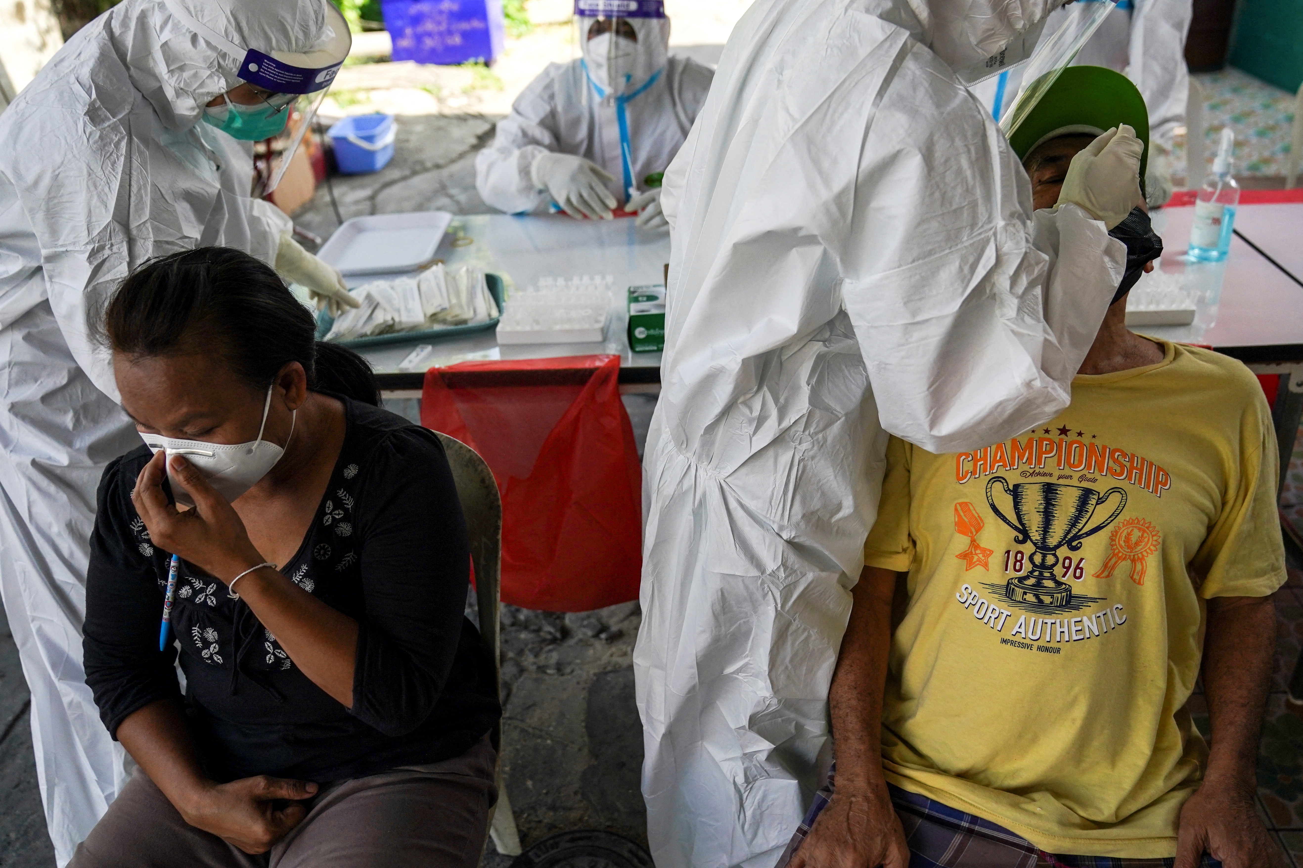 Healthcare workers in PPE take swab samples from people for a rapid antigen test, in Bangkok