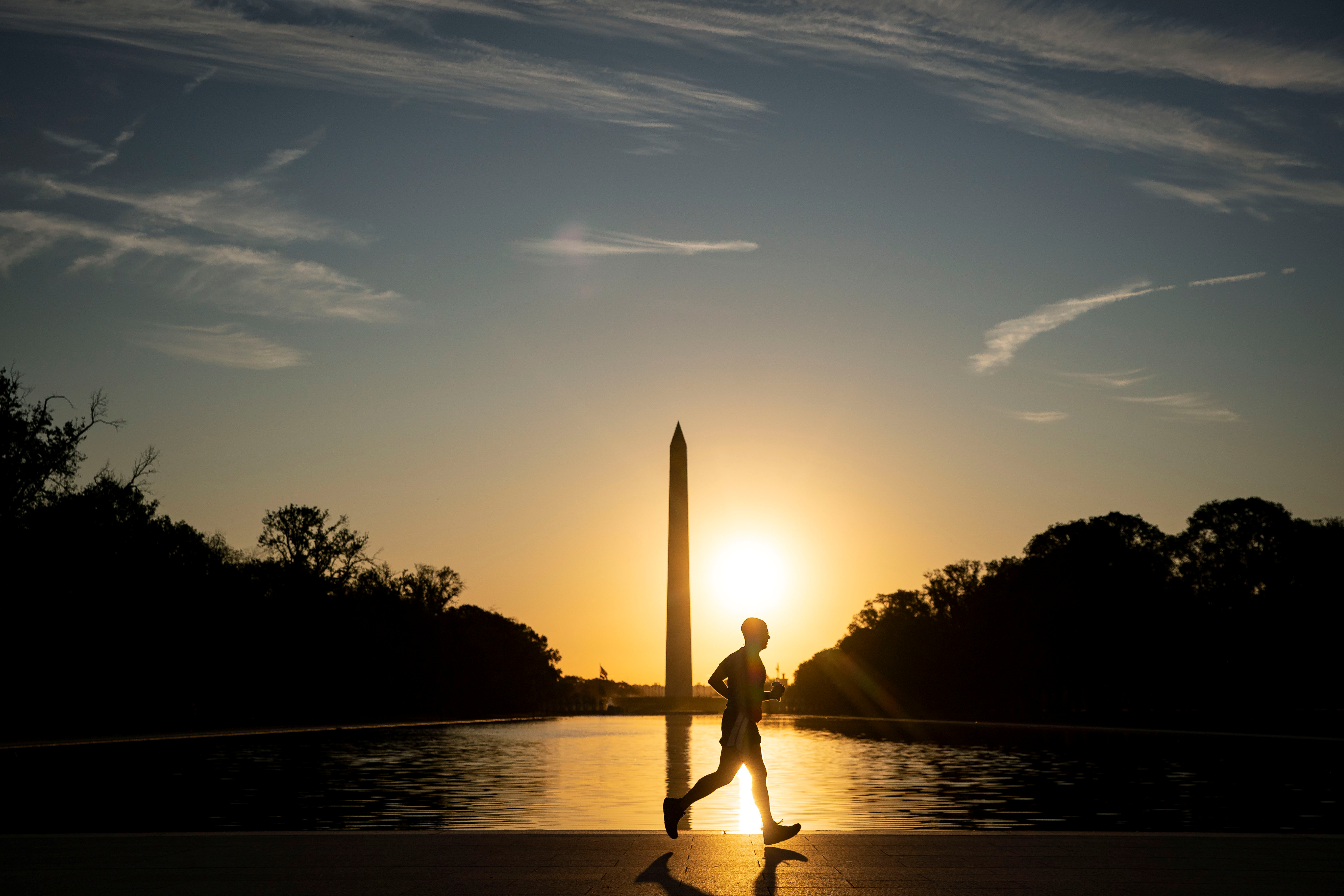 A man runs near the reflecting pool between the Lincoln Memorial and the Washington Monument at sunrise on the National Mall in Washington