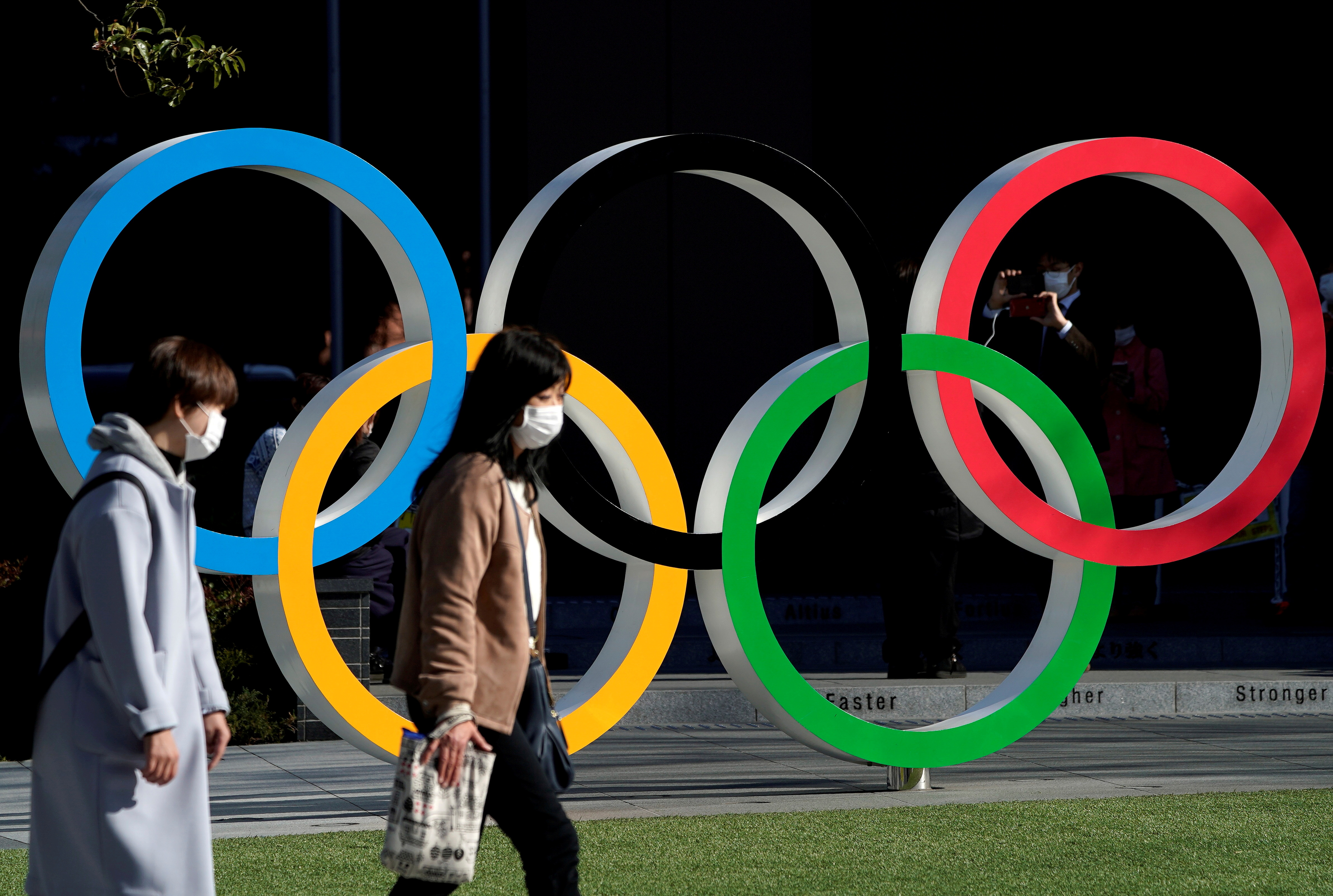 Women wearing protective face masks following an outbreak of the coronavirus disease walk past the Olympic rings in Tokyo