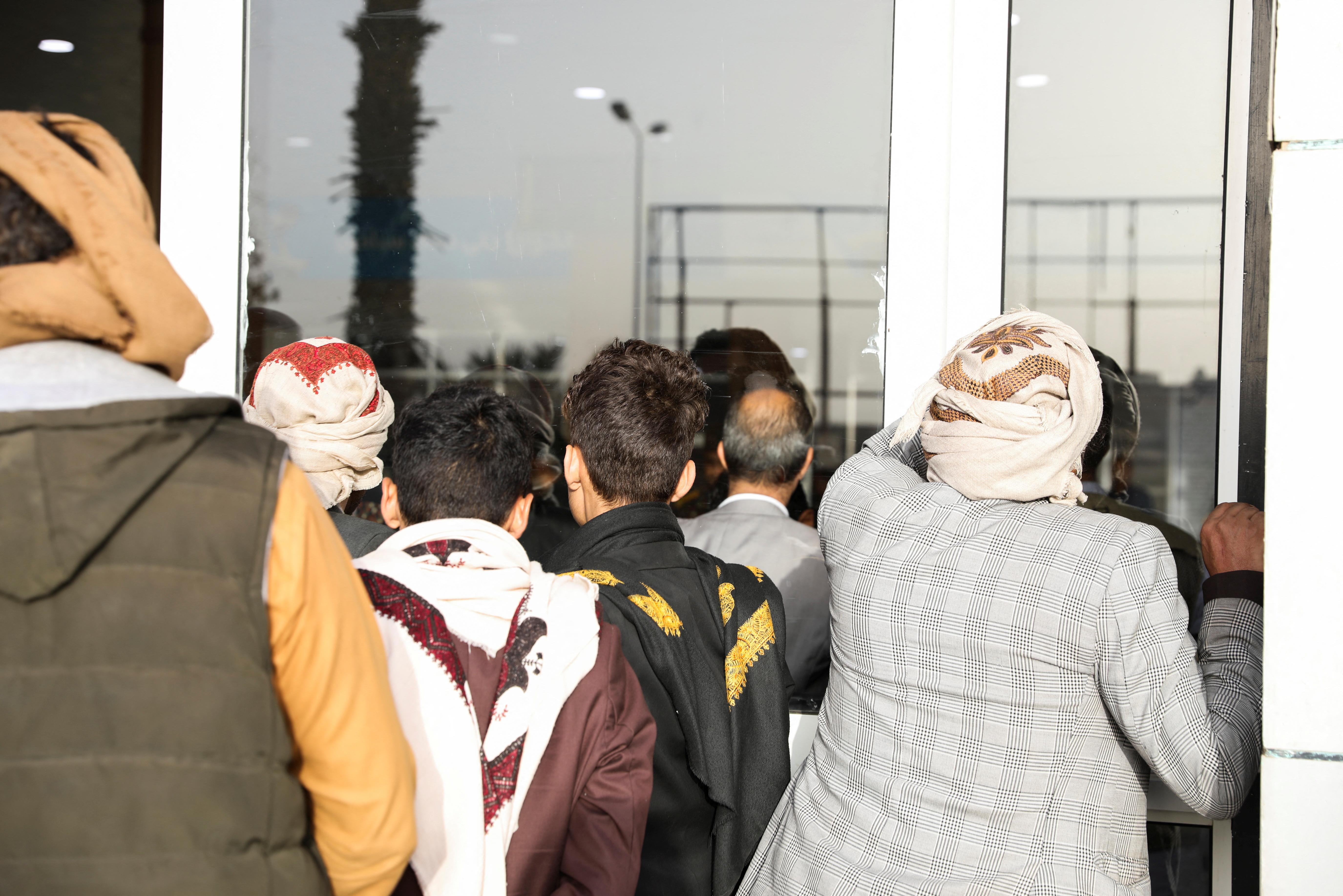 People look from behind glass doors at the departures lounge as passengers wait to board the first commercial flight to be operated from Sanaa Airport, in Sanaa
