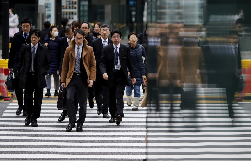 People are reflected on a wall as they cross a road at Tokyo's business district