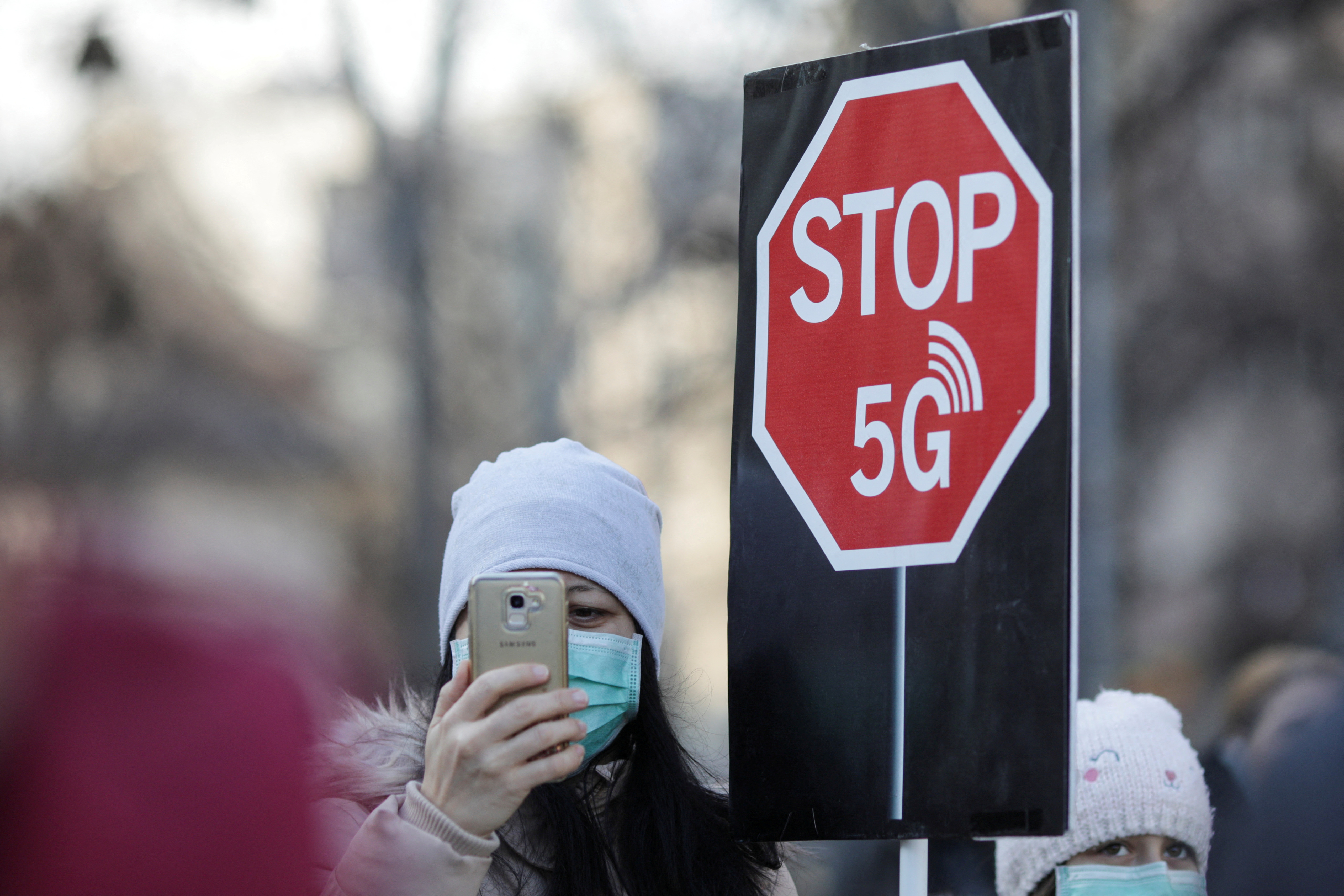 A woman uses her mobile phone while holding a placard reading " STOP 5G" during a protest against 5G technology