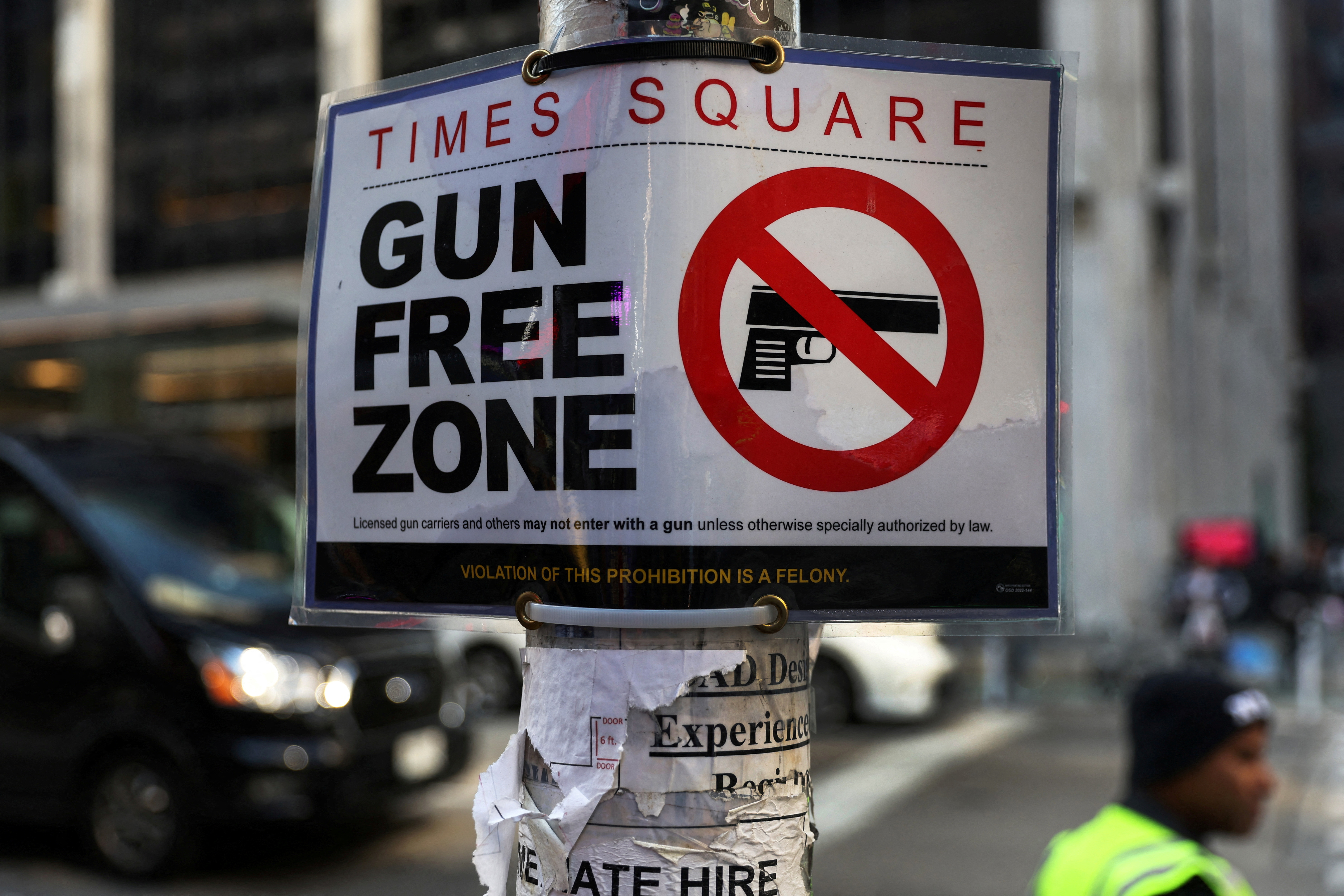 A Times Square Gun Free Zone sign hangs from a light pole on 6th avenue in New York City