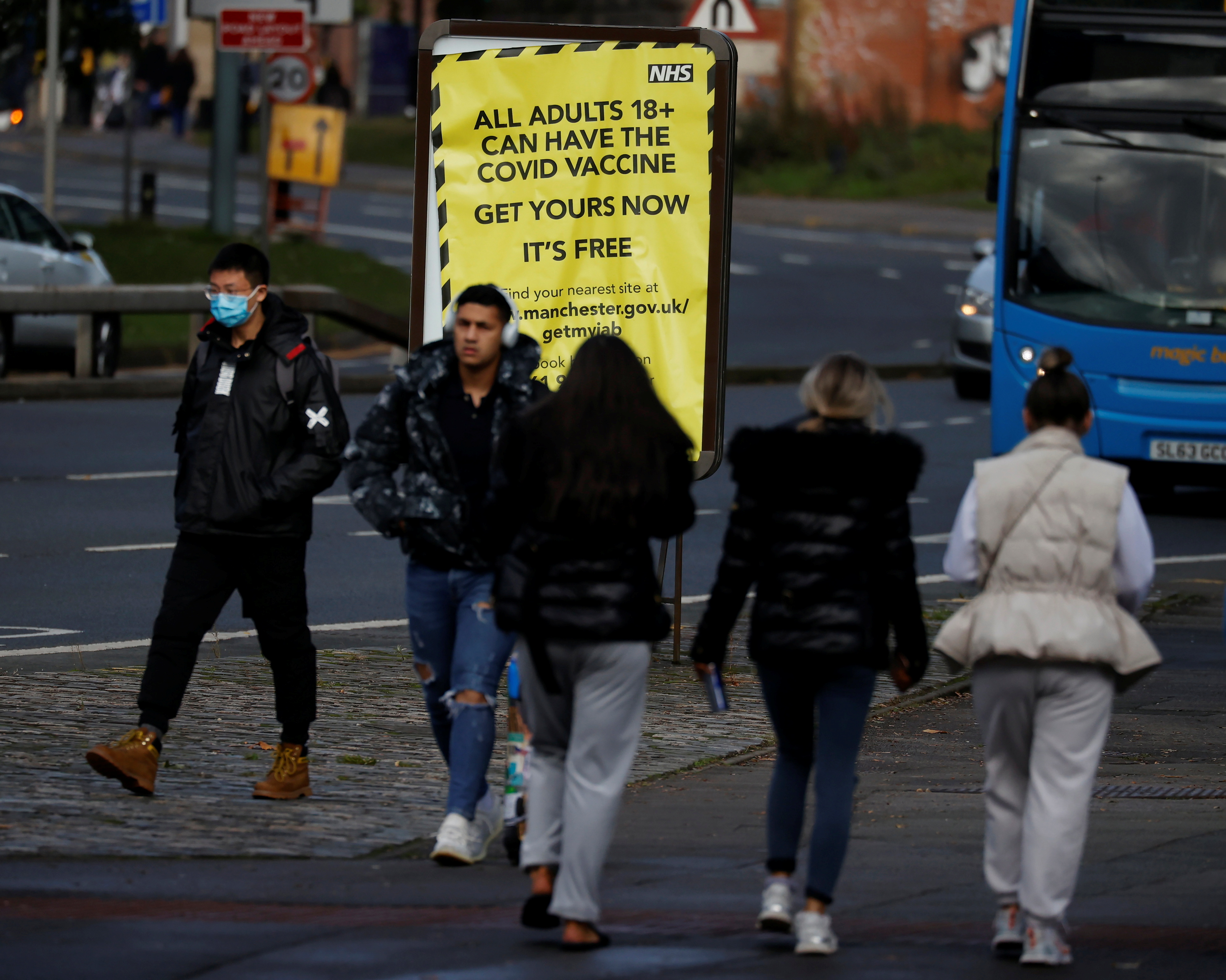 People walk past a sign encouraging the public to get their COVID-19 vaccine doses in Manchester