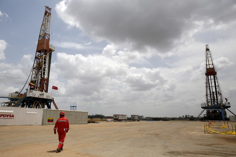 An oilfield worker walks next to drilling rigs at an oil well operated by Venezuela's state oil company PDVSA