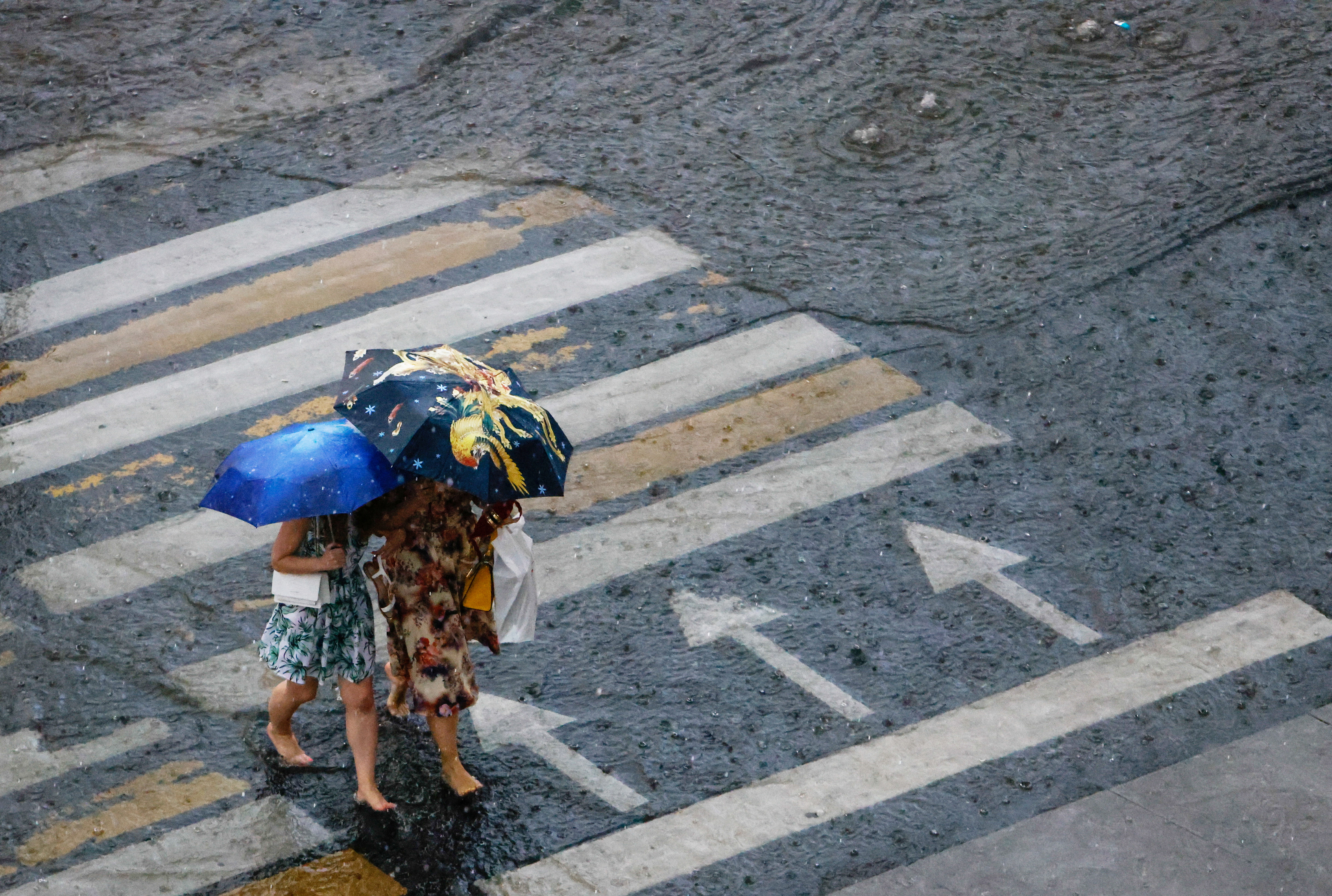 Women walk barefoot across the street during heavy rain in Moscow