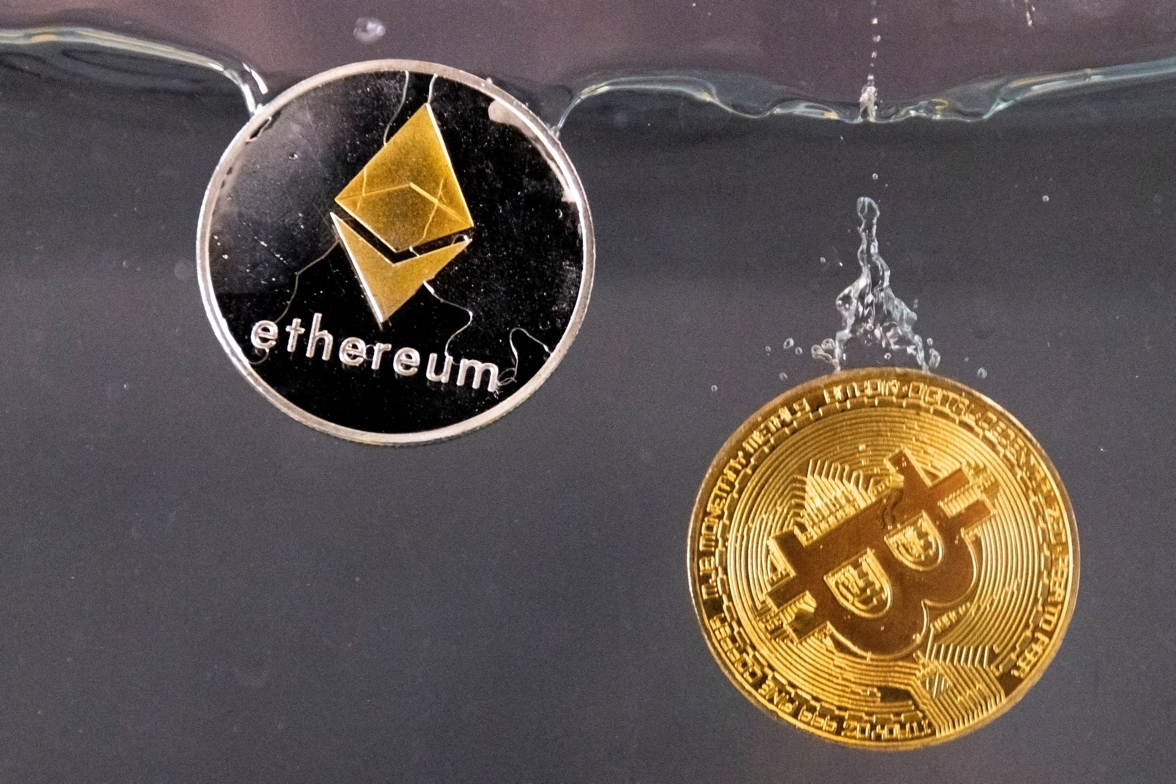 Bitcoin and Ether souvenir tokens fall into water