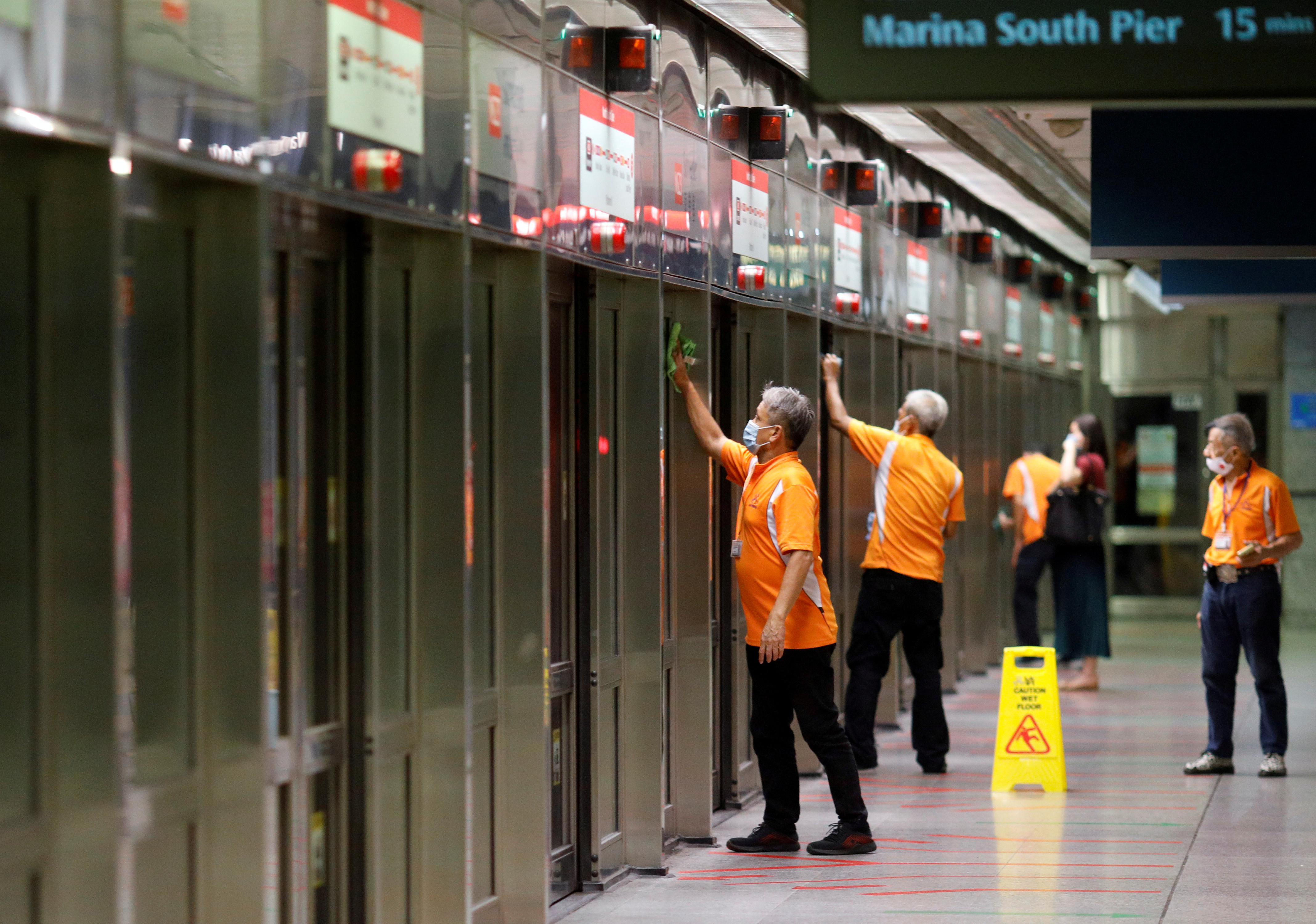 Workers wipe down doors at a train station during the coronavirus disease (COVID-19) outbreak in Singapore