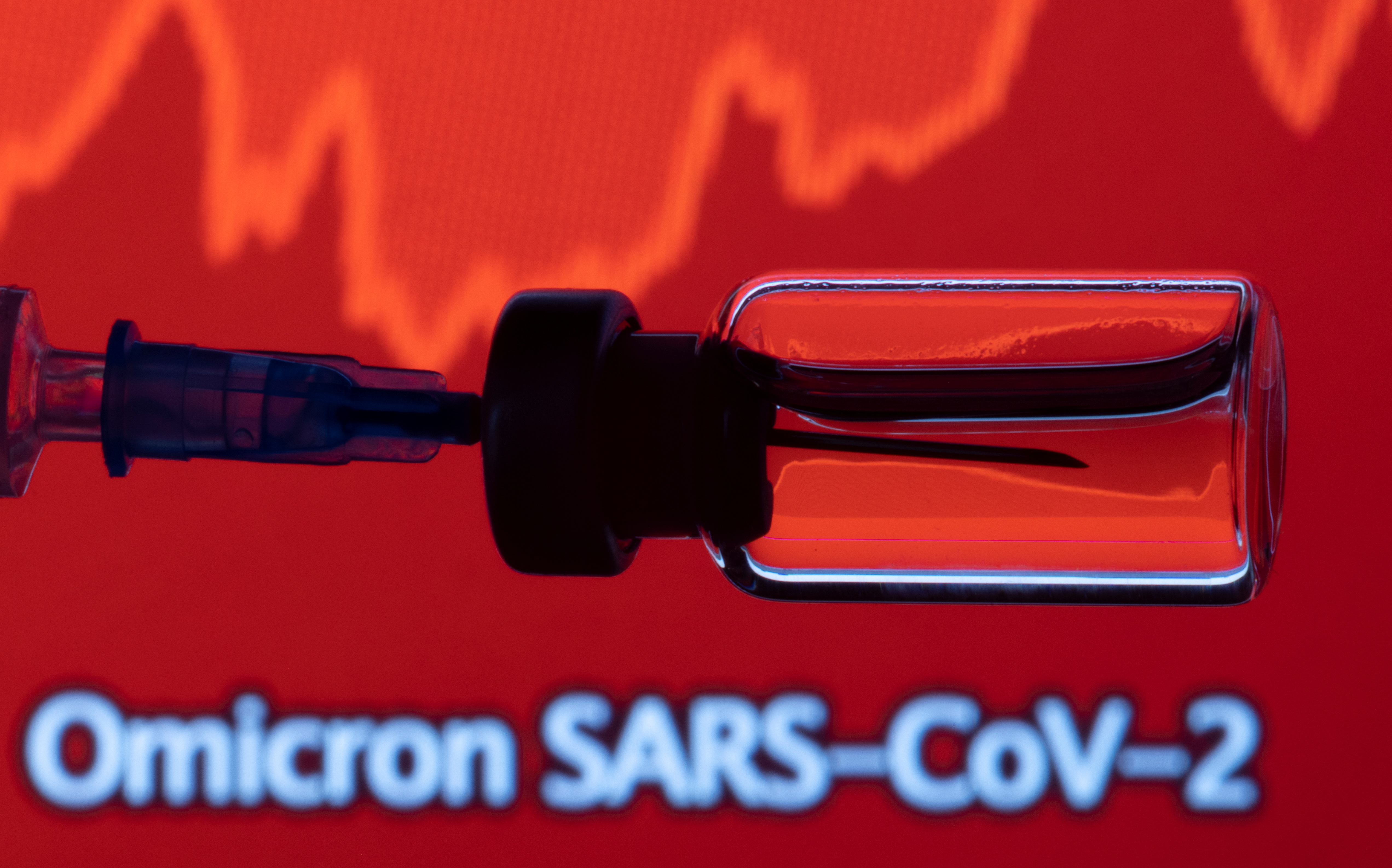 A vial and a syringe are seen in front of a displayed stock graph and words 