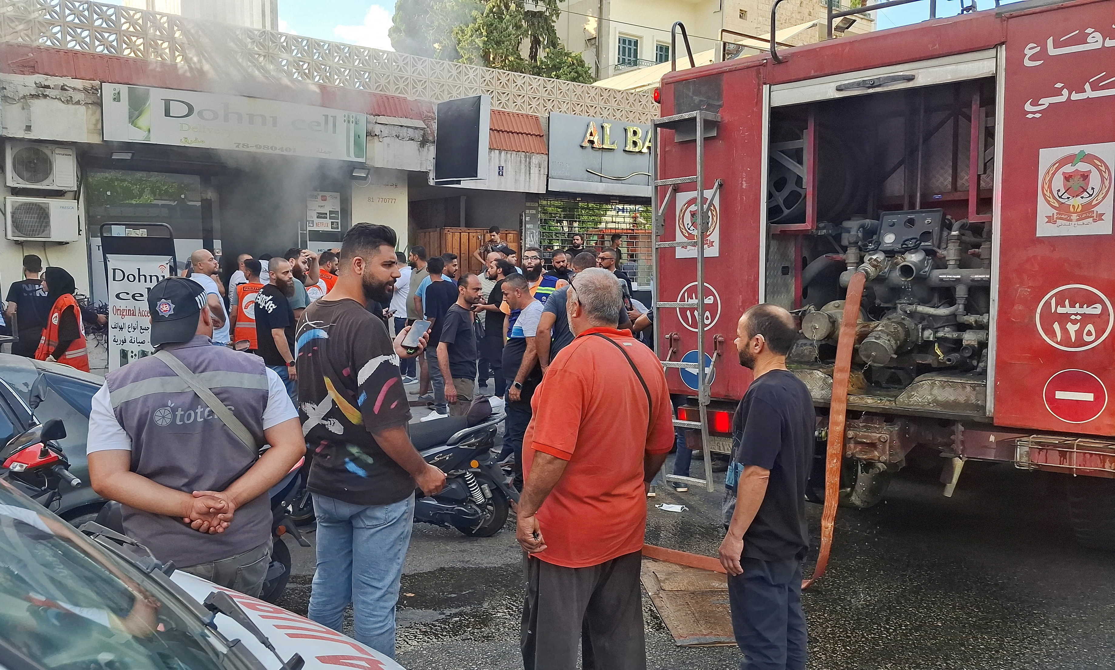 People gather as smoke rises from a mobile shop in Sidon