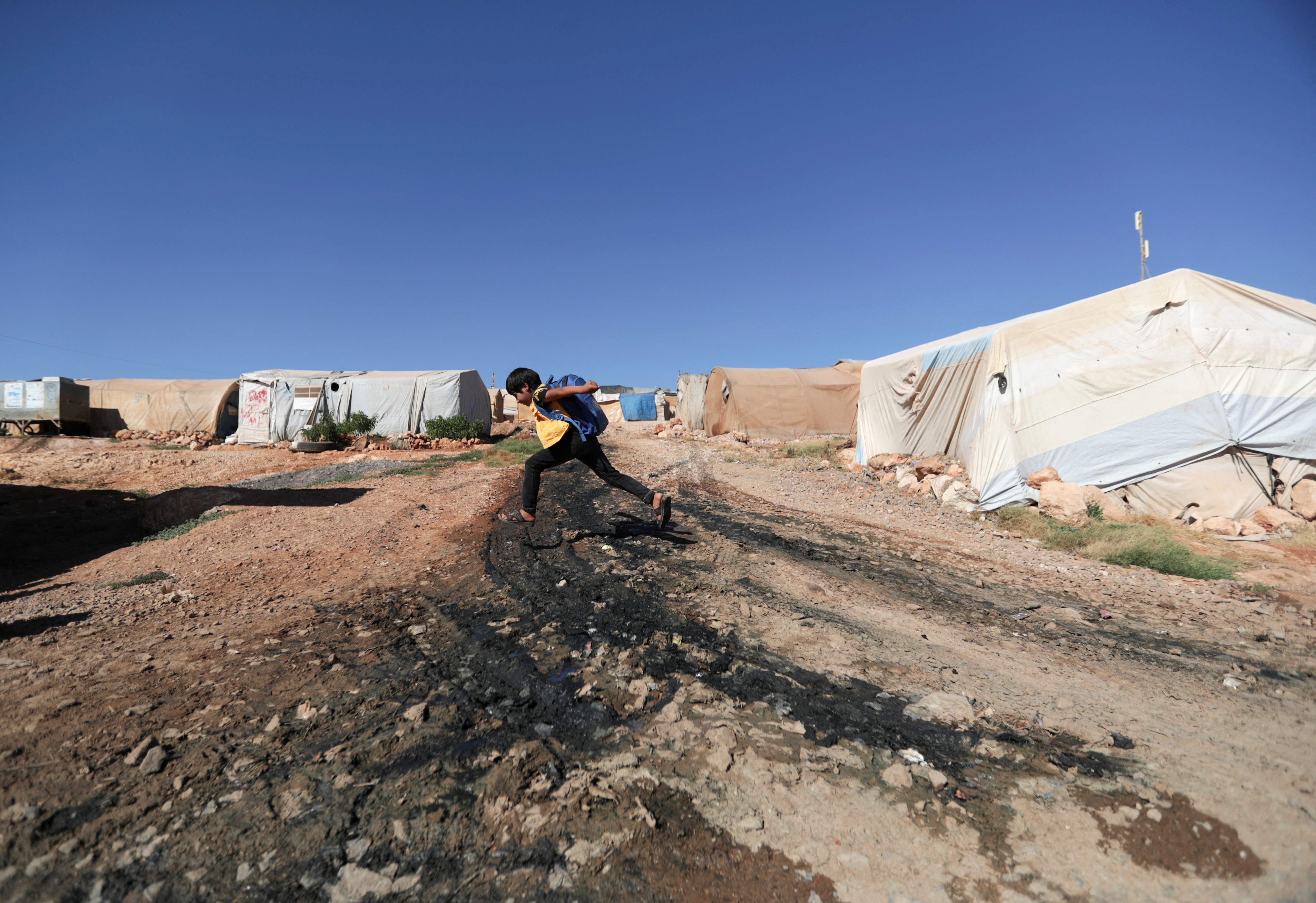 A boy jumps over sewage at a camp for internally displaced Syrians, in northern rebel-held Idlib