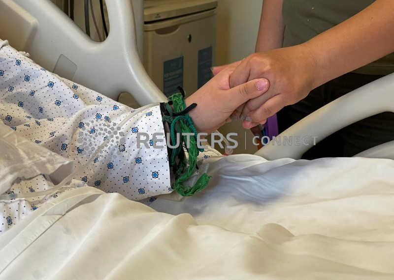 Liliane Cheaito, who is mostly paralyzed from August 2020 port blast holds her sister's hand in Beirut