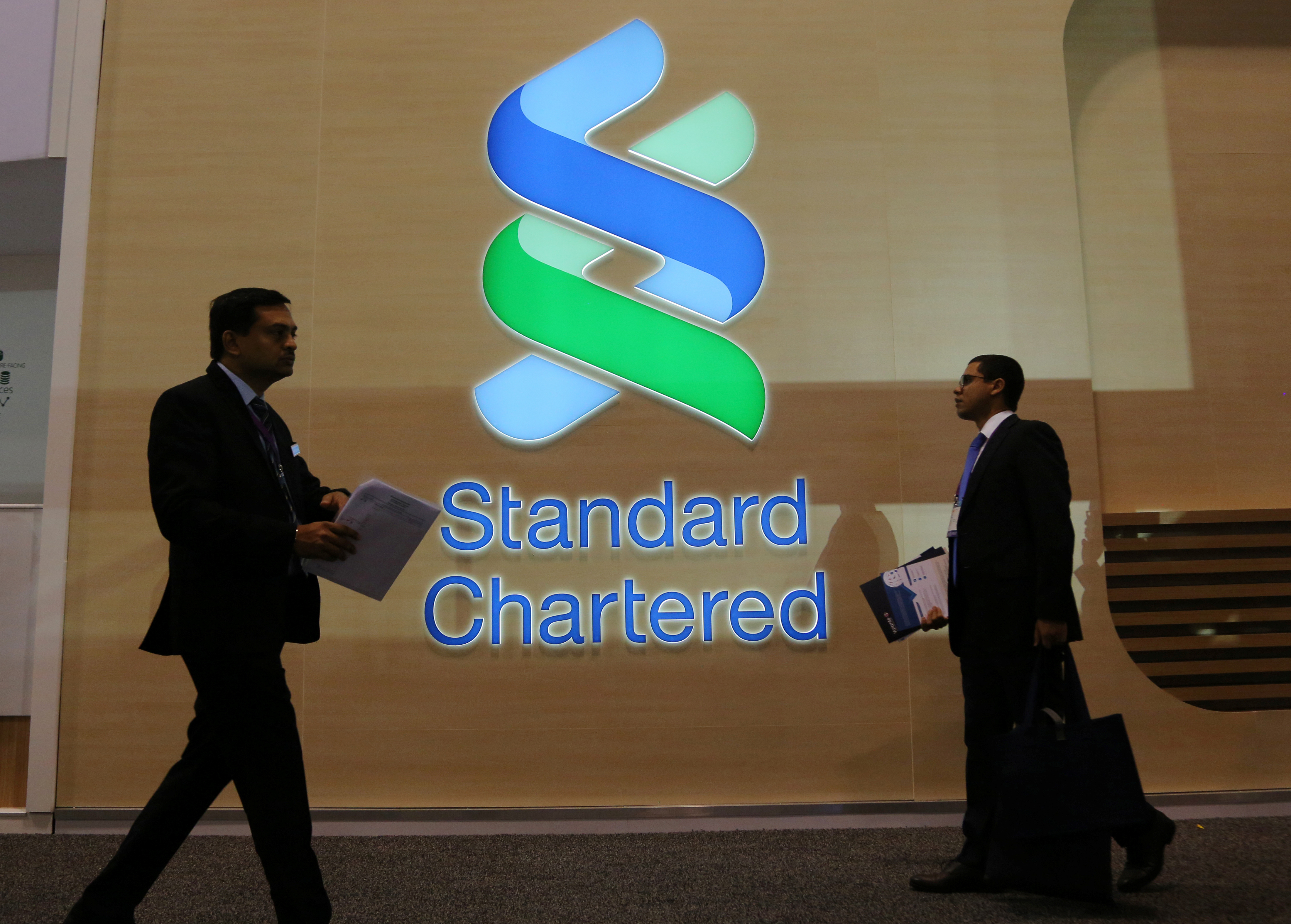 People pass by the logo of Standard Chartered plc at the SIBOS banking and financial conference in Toronto