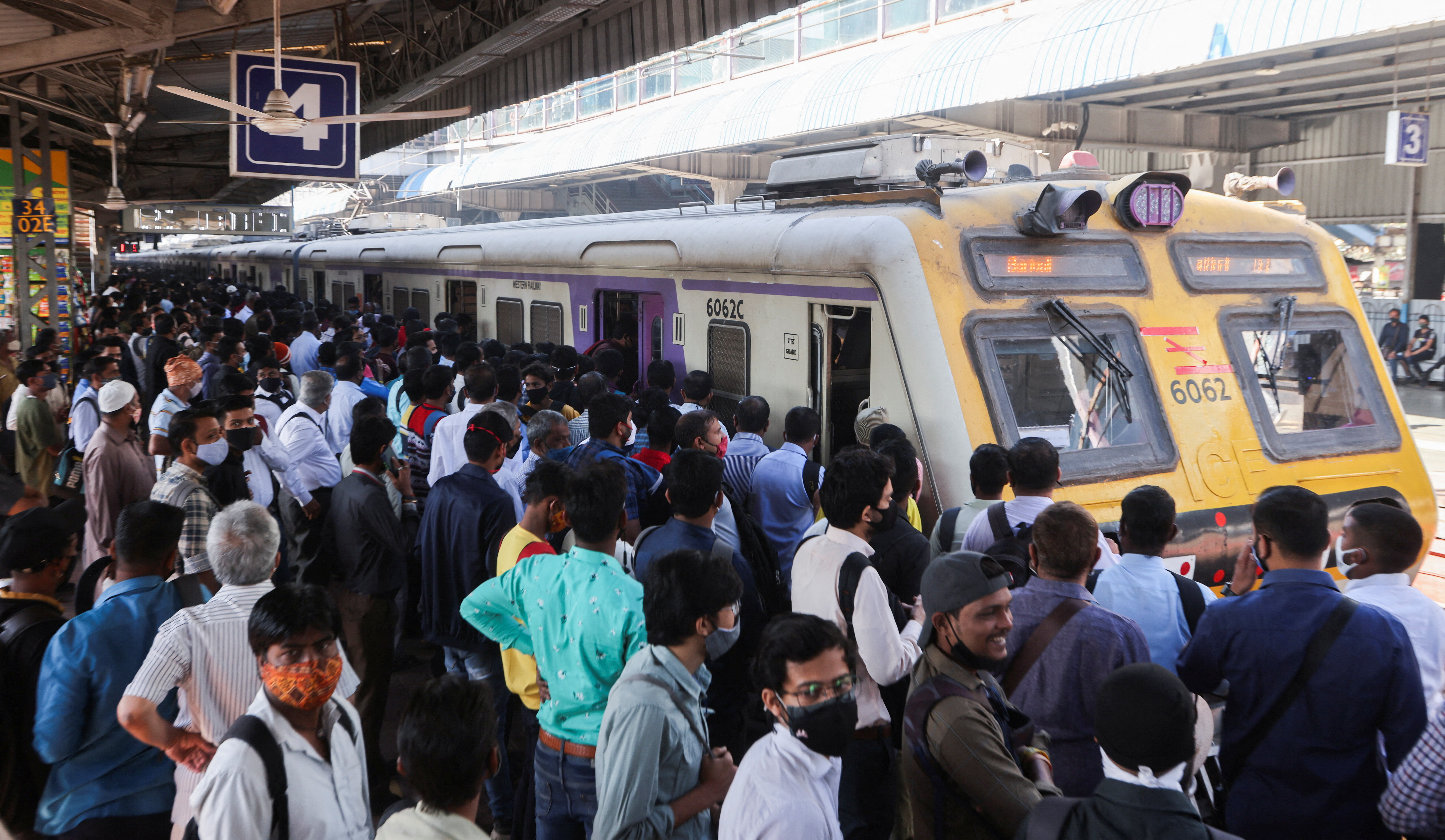 Commuters wait to board a train at a railway station in Mumbai