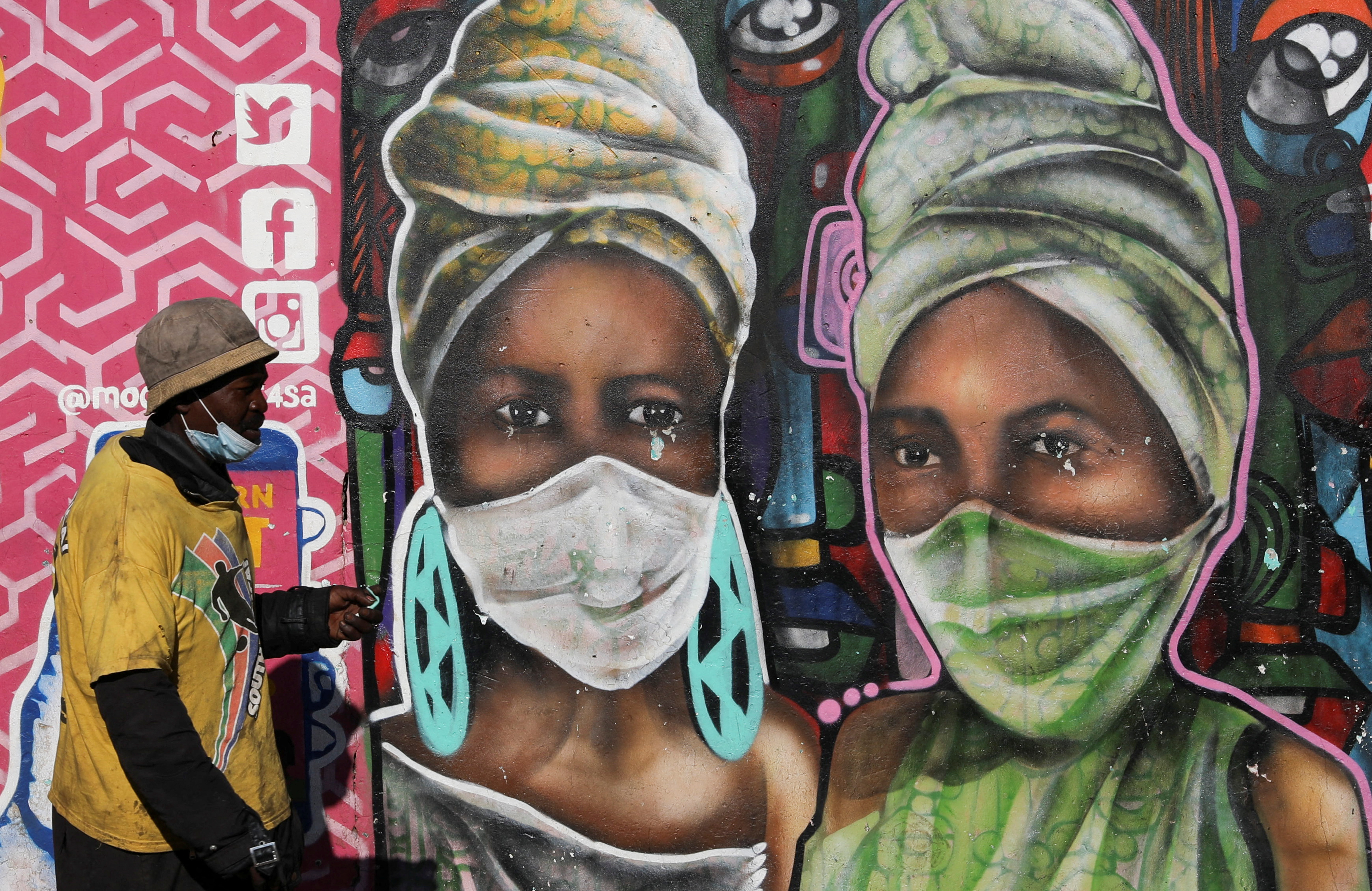 A man walks past a mural by Senzart911 that shows people wearing facemasks, as South Africa scraps isolation for coronavirus disease (COVID-19) positive people with no symptoms, at Soweto's Kliptown, South Africa, February 1, 2022. REUTERS/Siphiwe Sibeko 