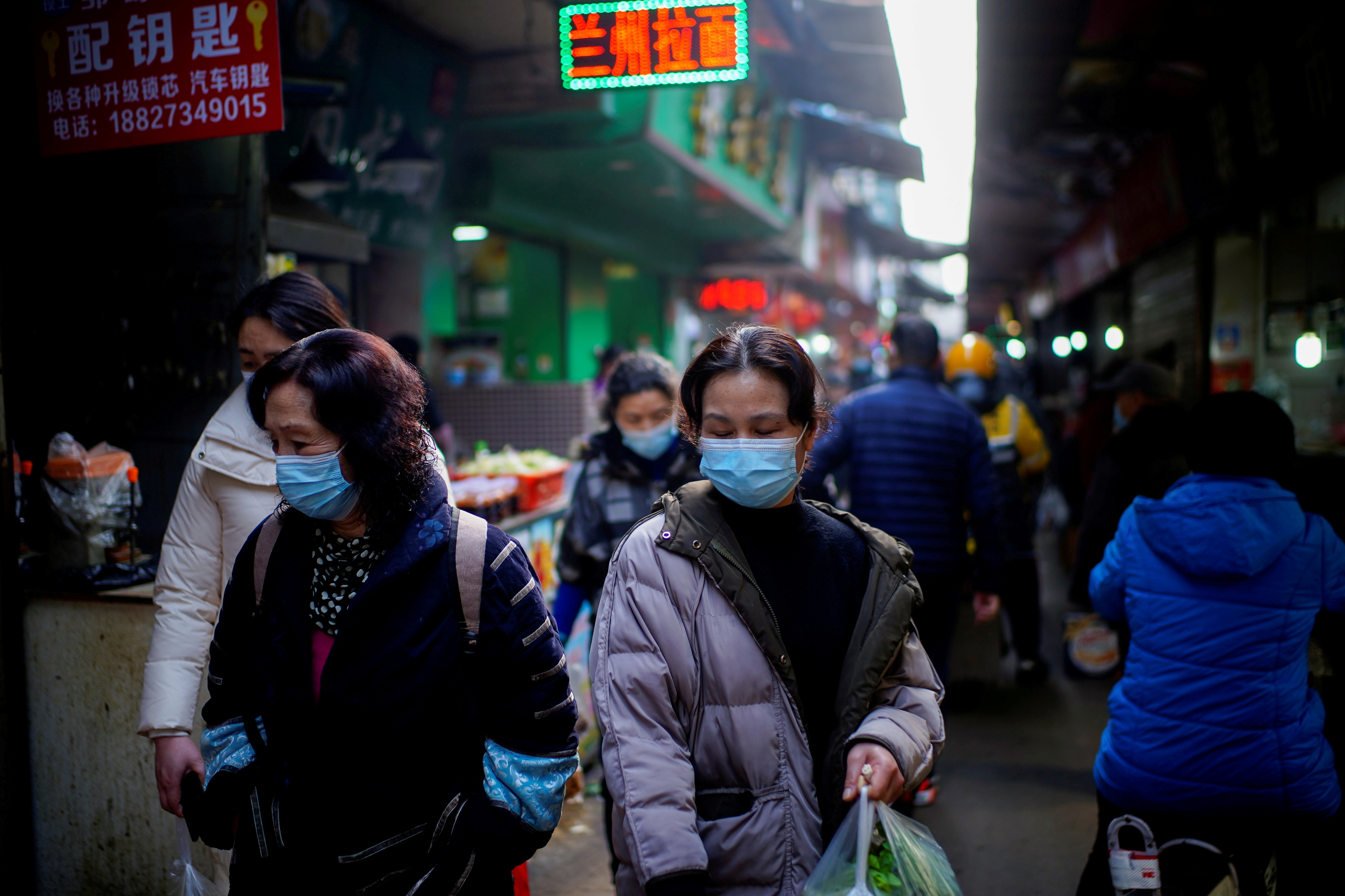 FILE PHOTO: People wearing face masks walk on a street market, following an outbreak of the coronavirus disease (COVID-19) in Wuhan