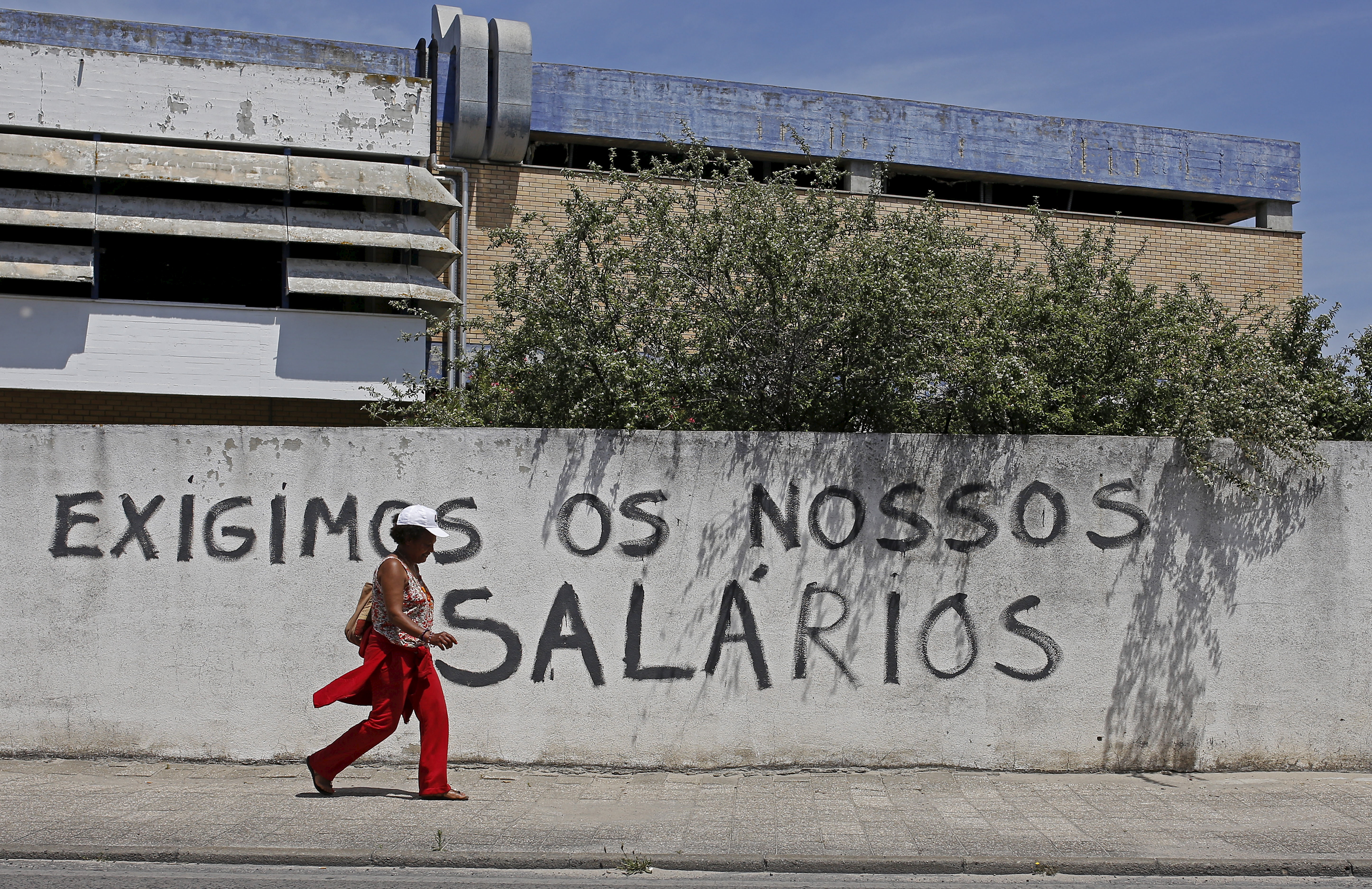 A woman walks past a wall with graffiti saying 