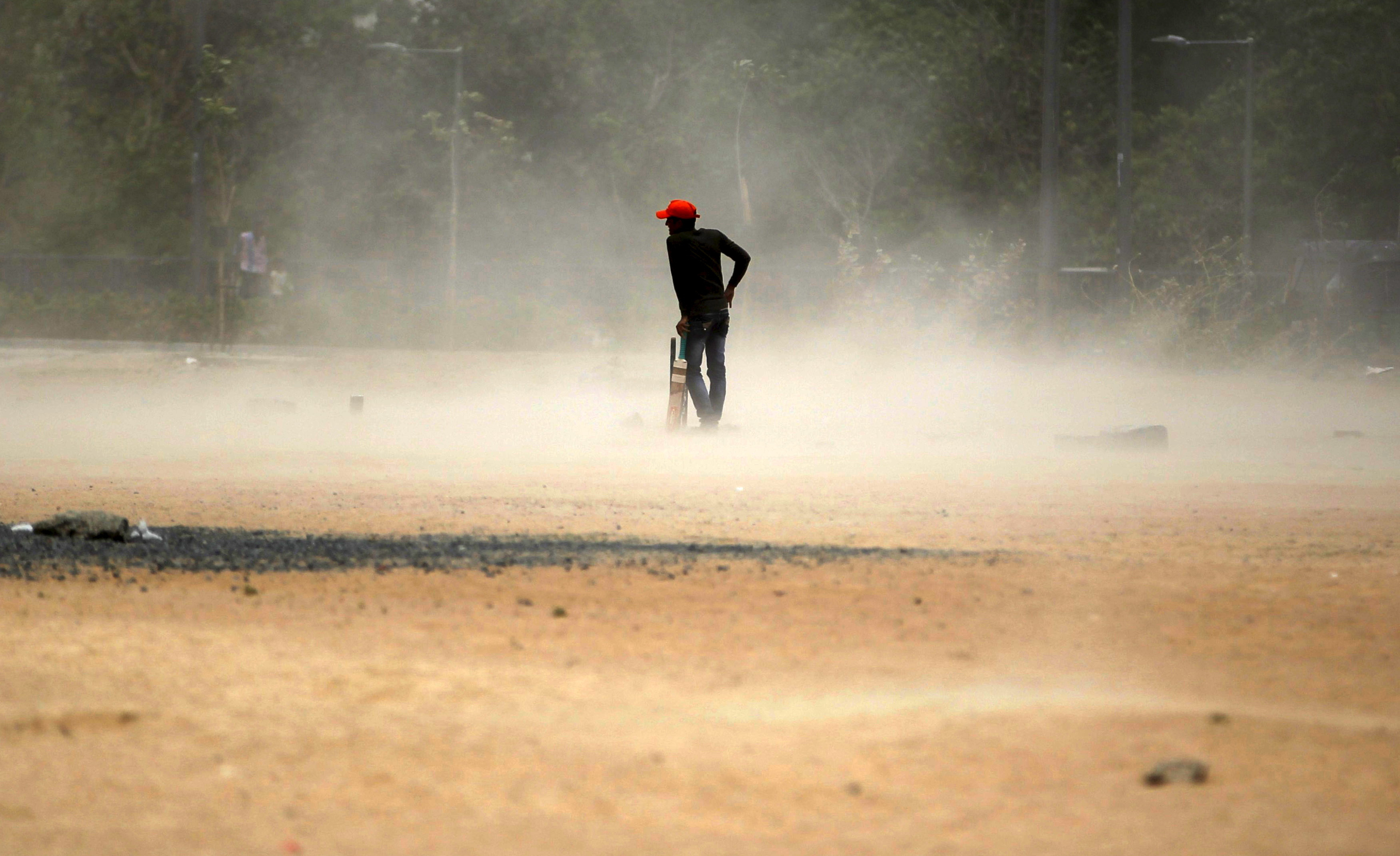 A boy waits for a brief dust storm to pass while playing cricket on a hot day in Ahmedabad