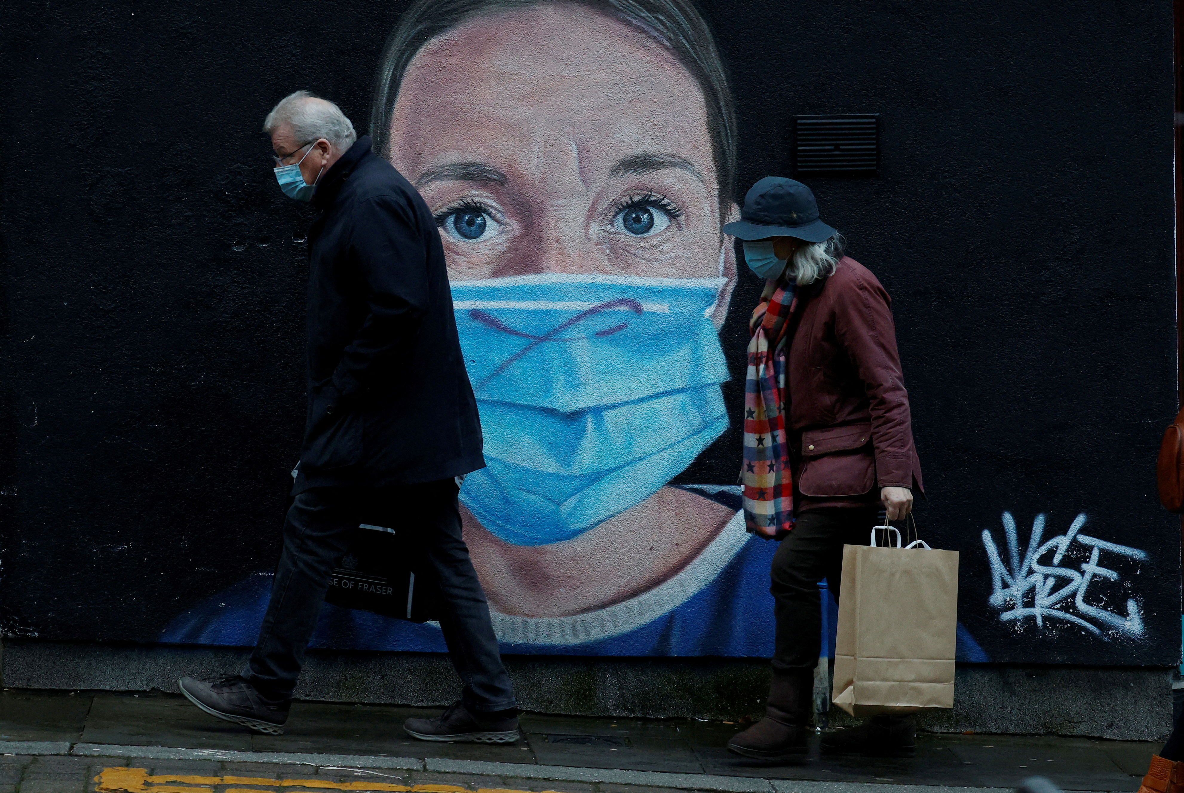 People wearing face masks walk past a mural of a nurse in the centre of Manchester