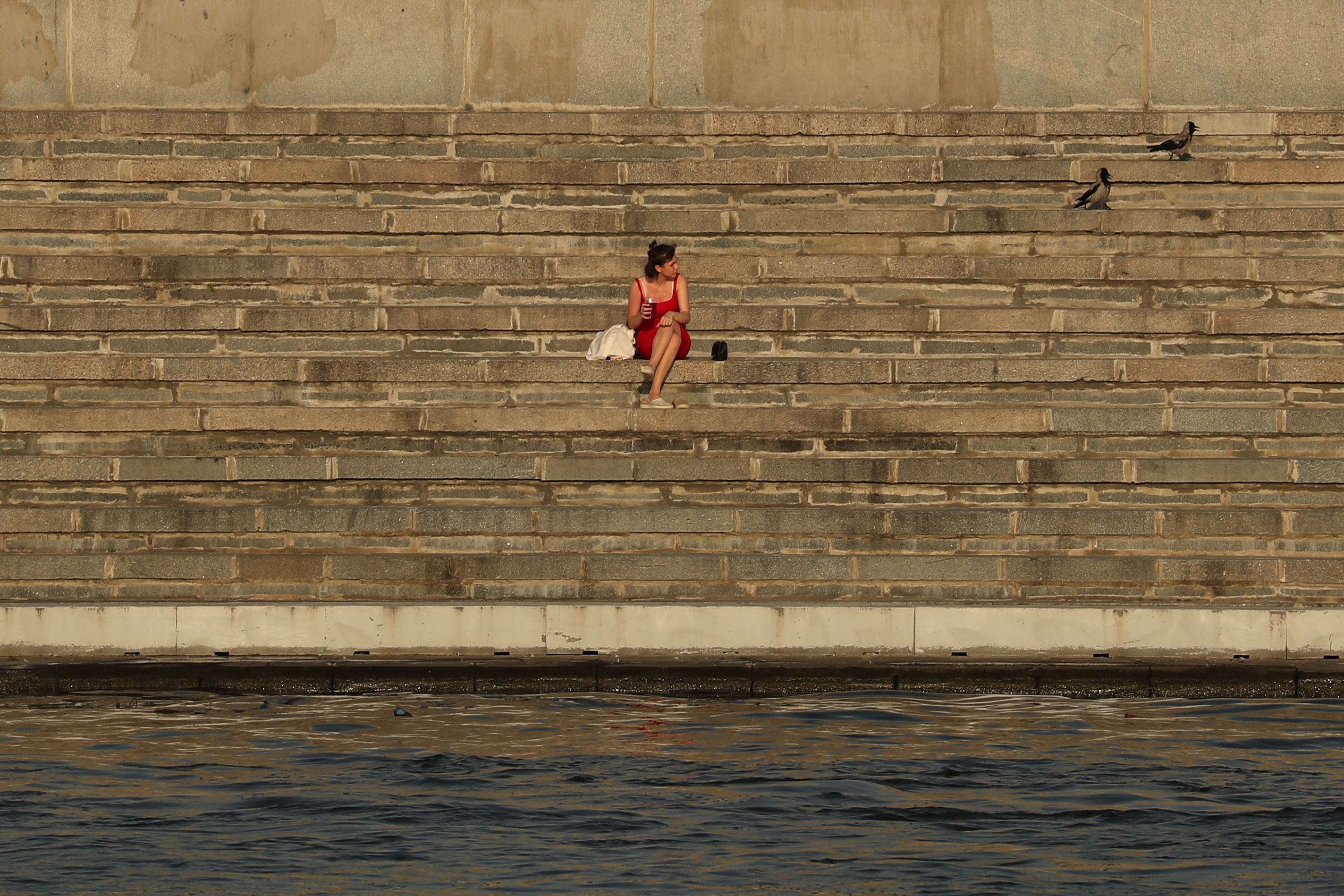 A girl seats next to the Moskva River on a hot day in Moscow